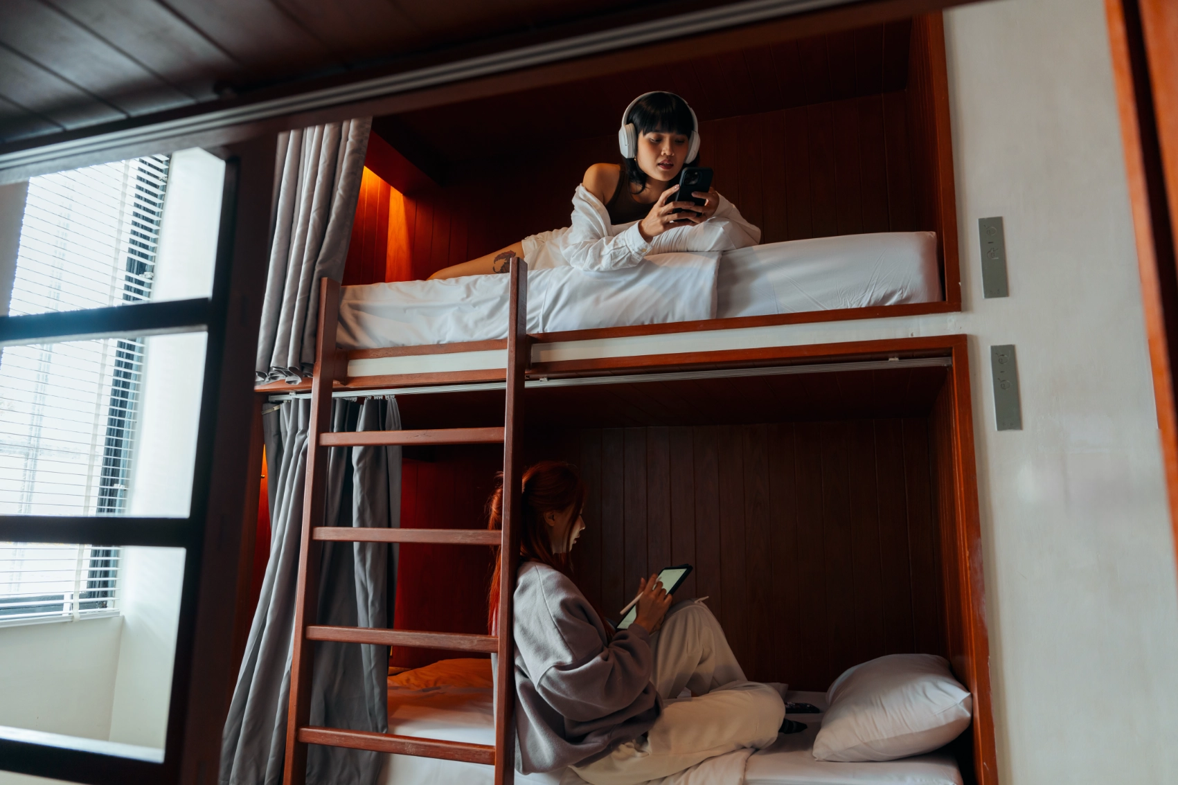 Sustainable accommodations Two women travellers sit on different bunks in a hostel