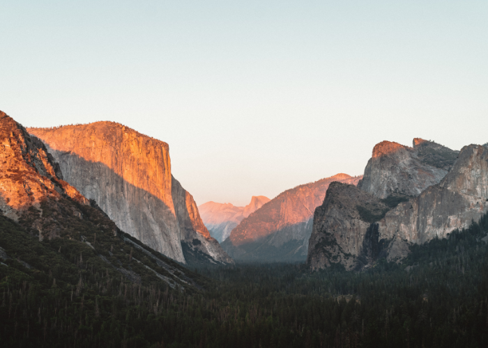 a peachy pink moment as the setting sun illuminates the granite monoliths of El Capitan and Half Dome in Yosemite National Park