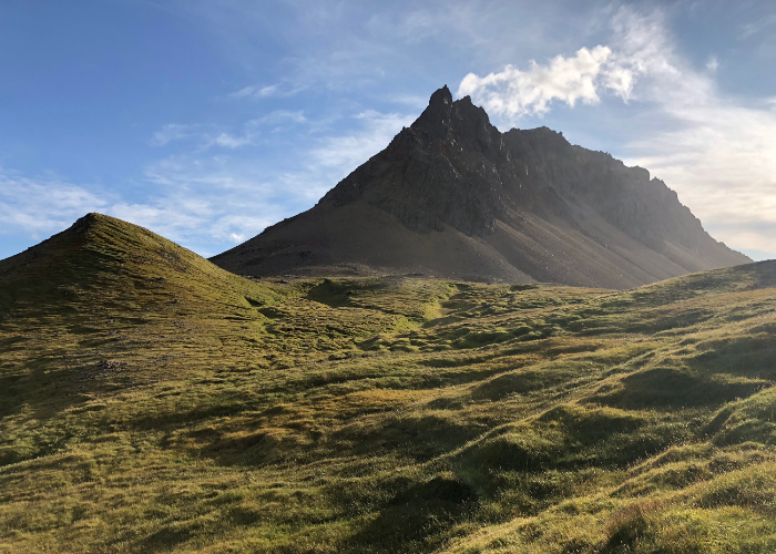 a jagged peak in the distance with the green mountains of Brúnavík Pass in the foreground from a hike in East Iceland