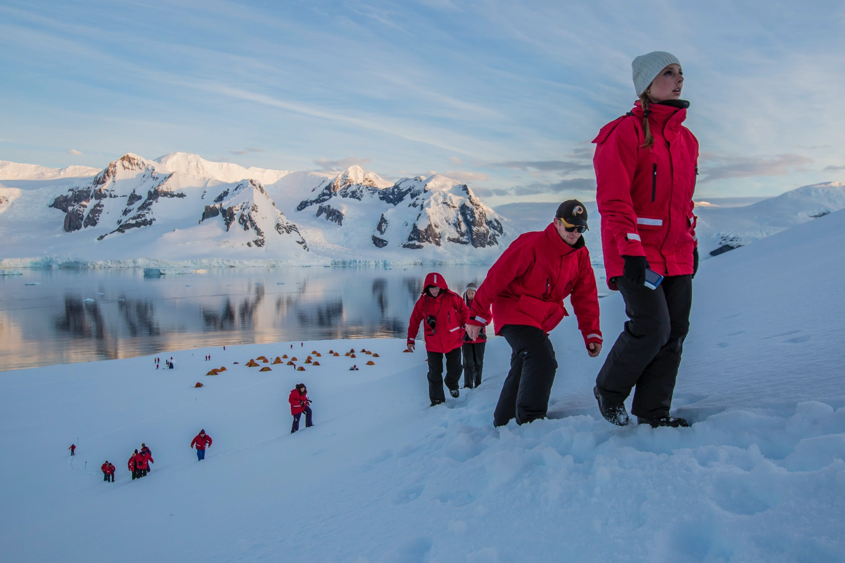 A group of travellers wearing red parkas hike in the snow in Antarctica