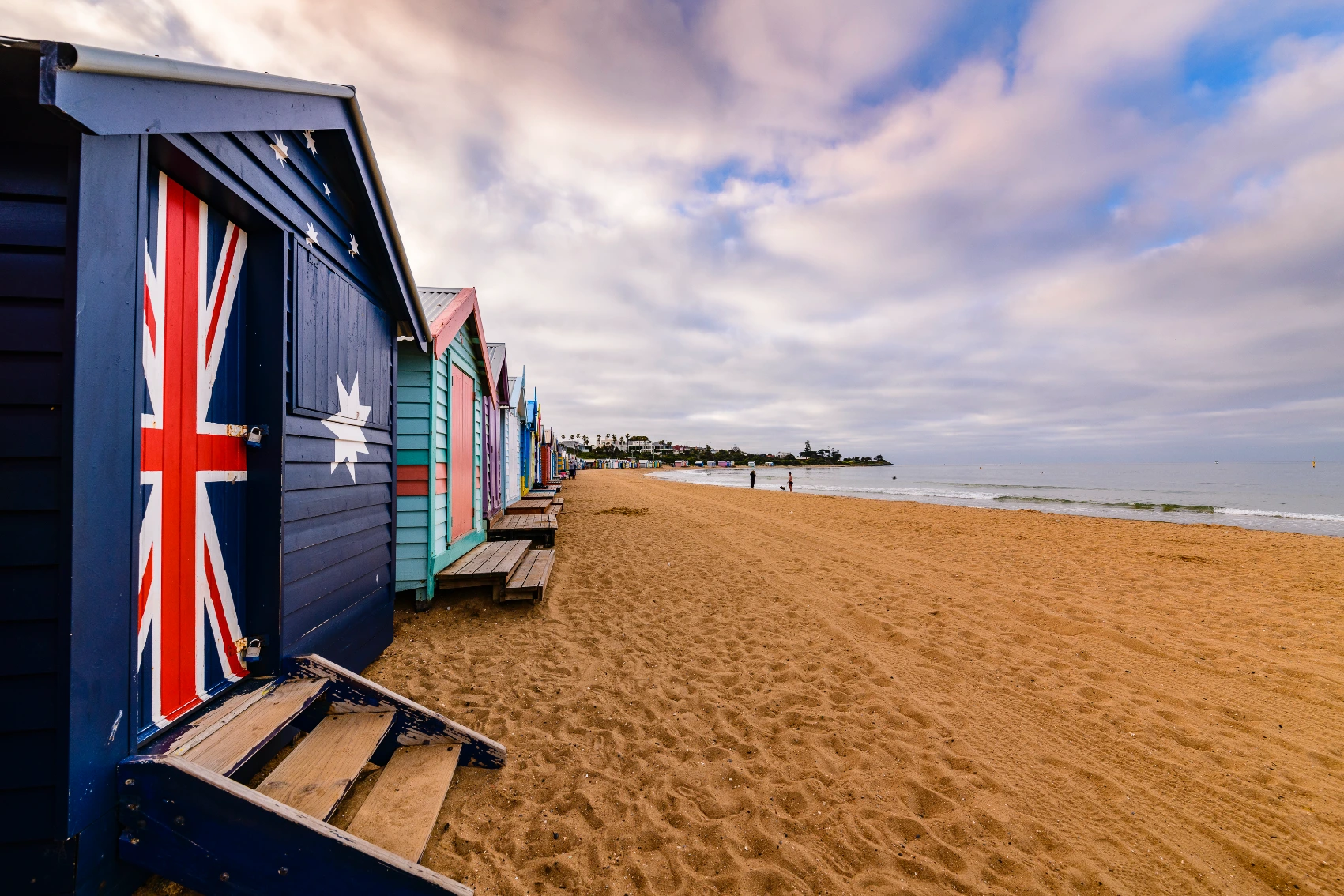 A row of colourful beach huts with people walking in the distance on Brighton Beach, Australia