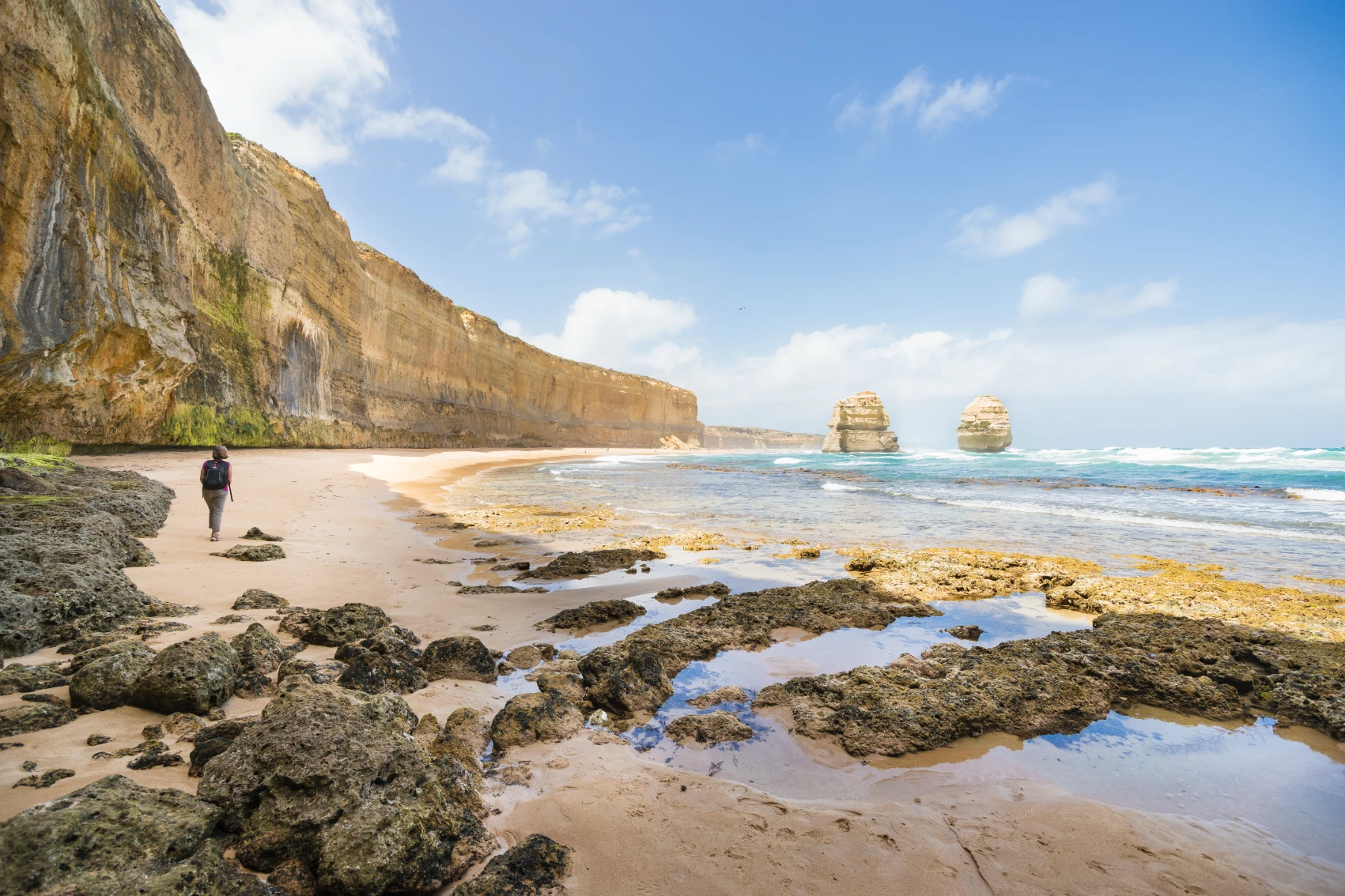 A woman traveller walks on a beach near rock formations on the Great Ocean Road in Australia