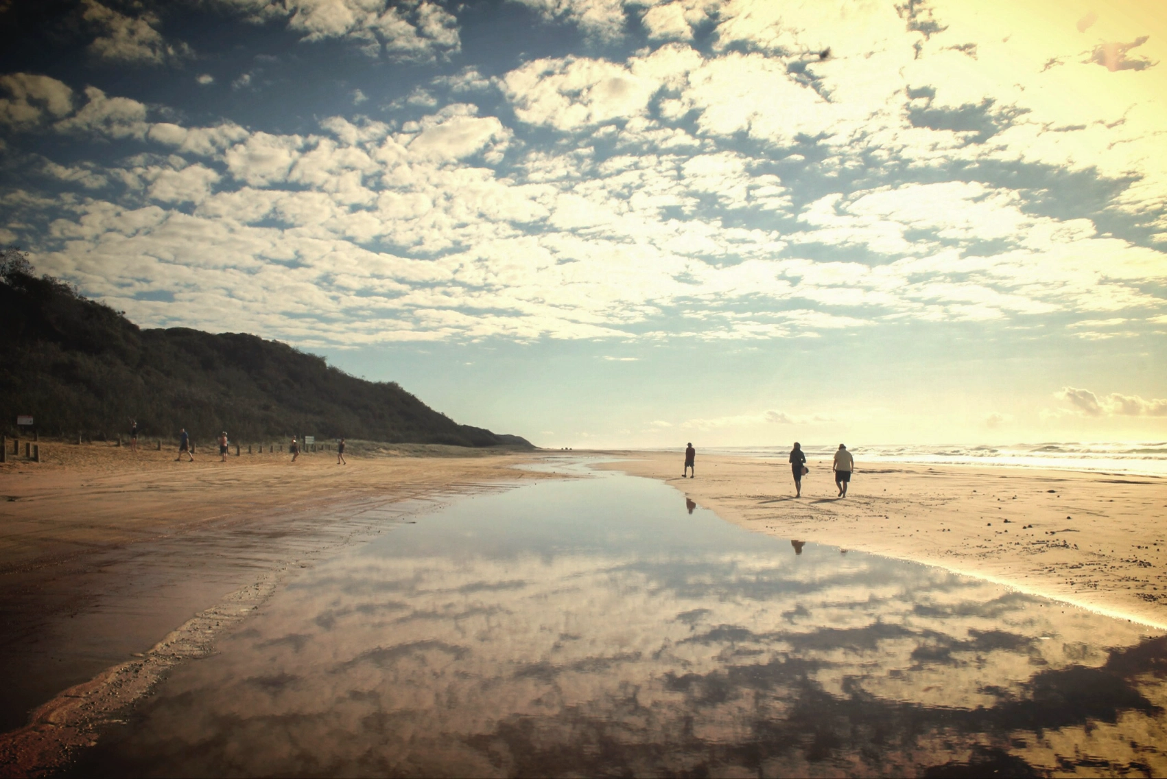 Travellers walk along a beach in K'gari, Australia