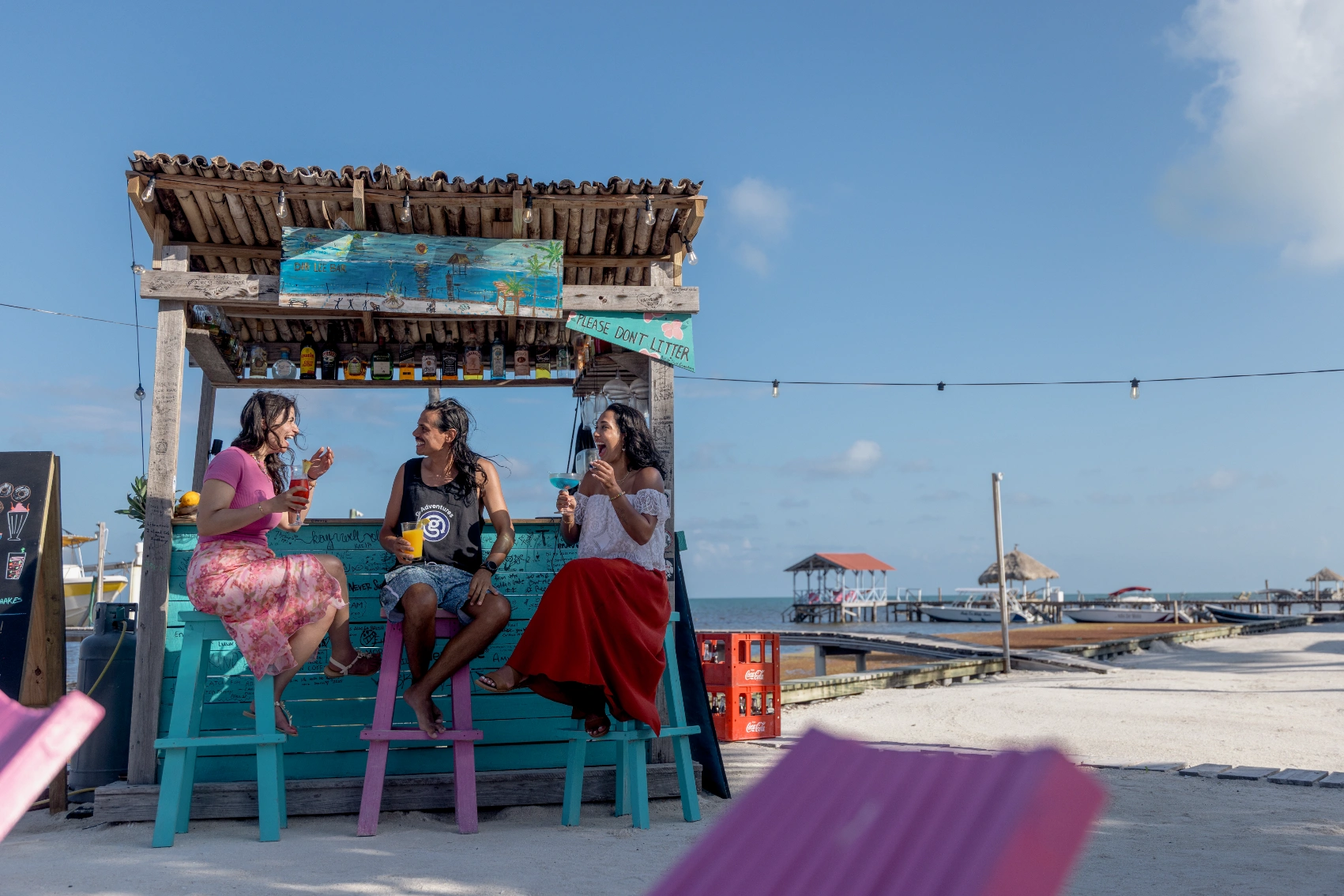 Three travellers sip cocktails on bar stools at an outdoor bar on Caye Caulker, Belize
