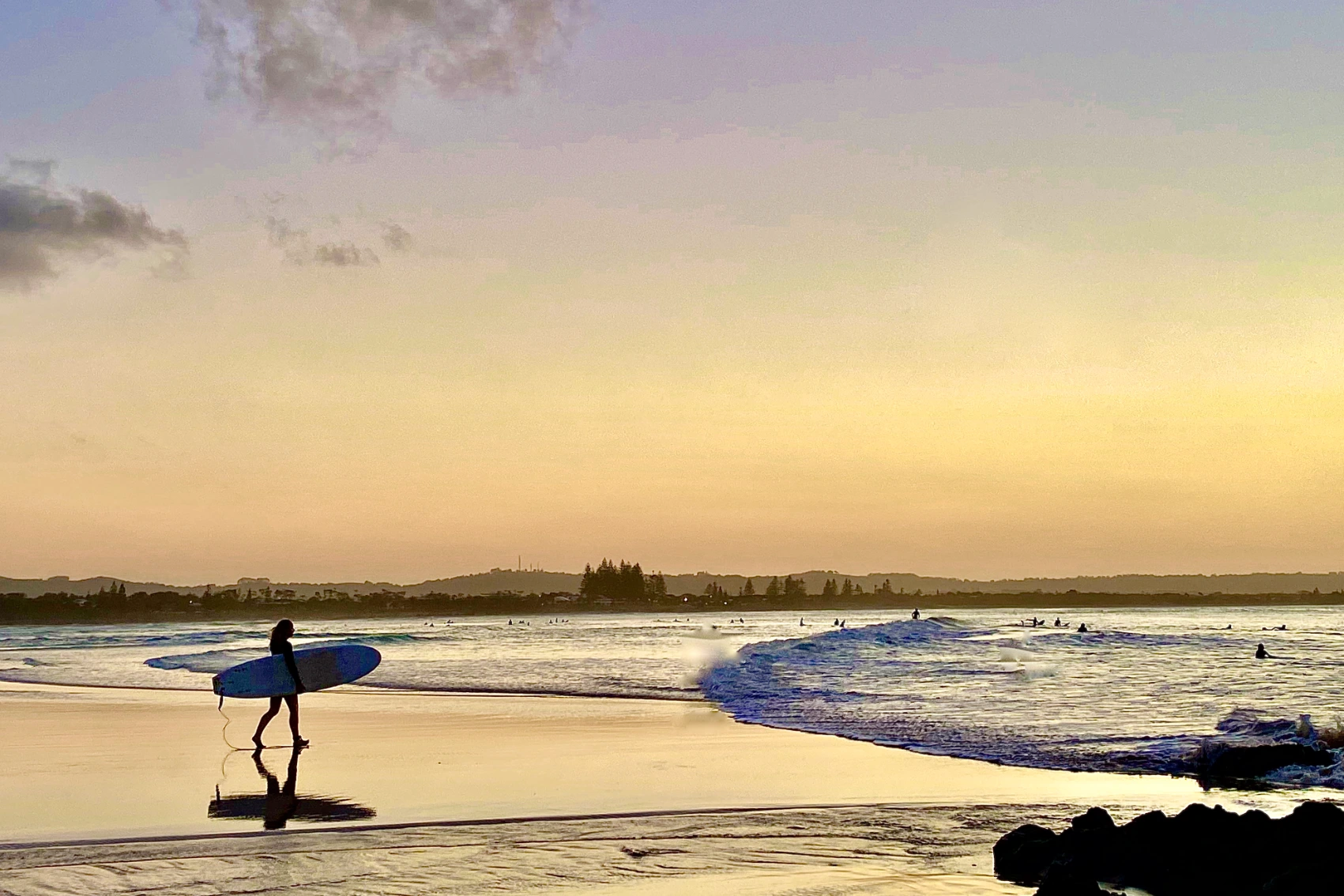 A surfer walks on the beach at sunset in Byron Bay, Australia