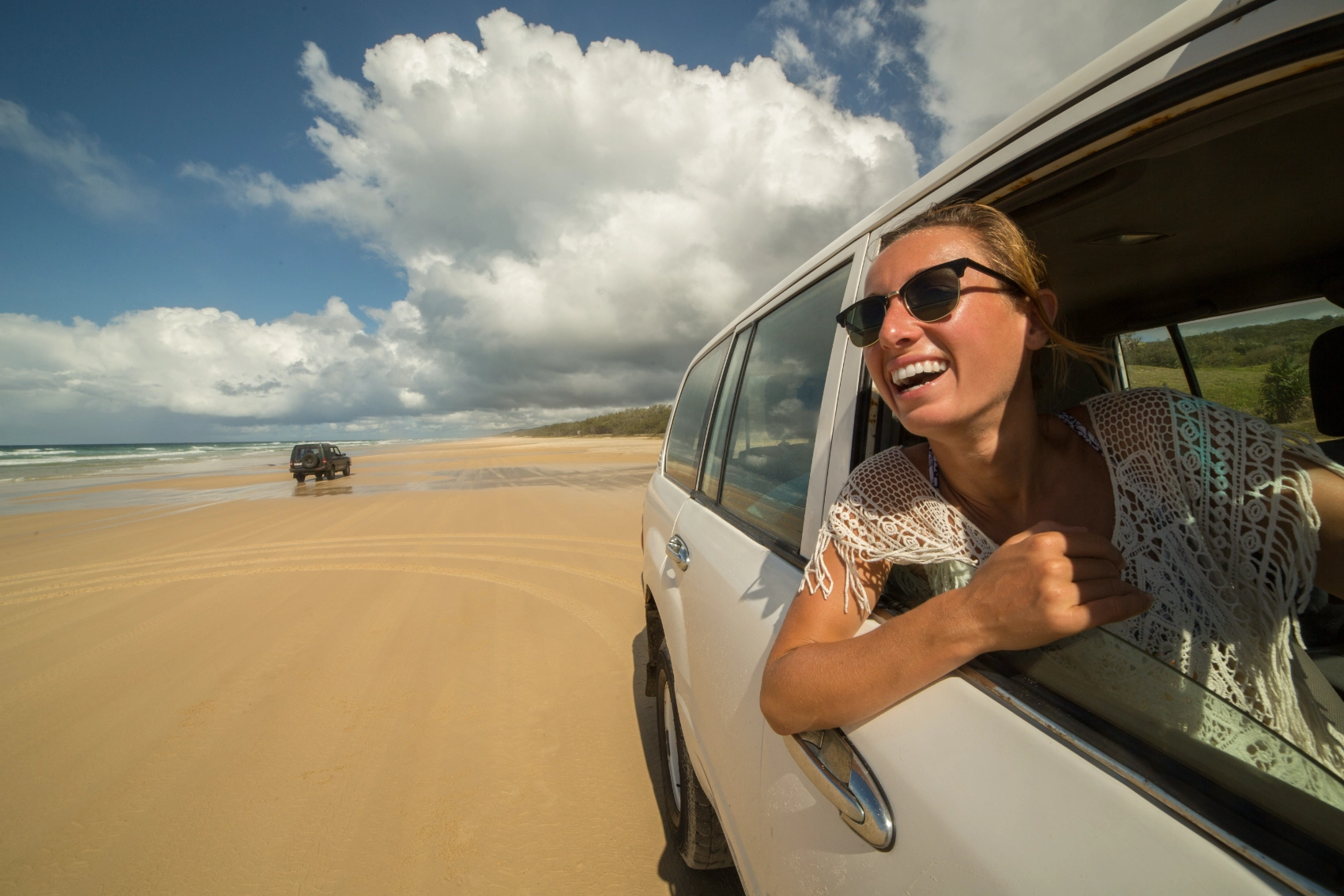 A woman leans out the window of a 4x4 driving on the beach in K'gari, Australia