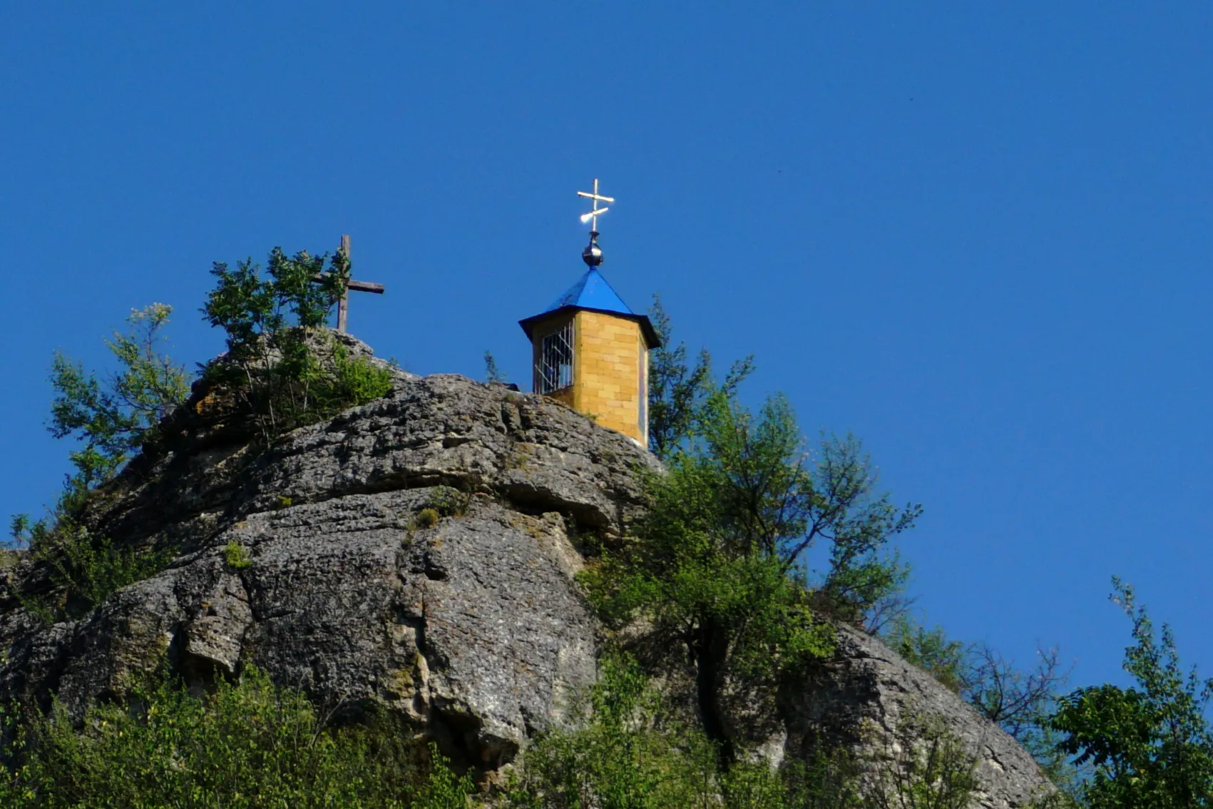 A small blue monastery with a cross sits atop the cliffs at Saharna Monastery in Moldova