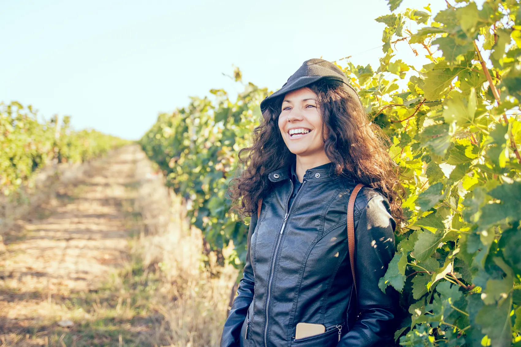 A cool female traveller in a leather jackets smiles as she stands in front of Moldovan grape vines