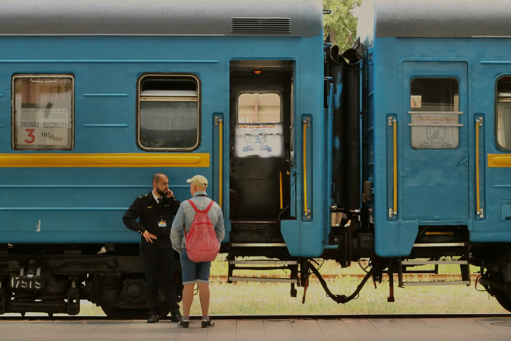 A male traveller with a backpack chats to a train attendant at a Moldova train station