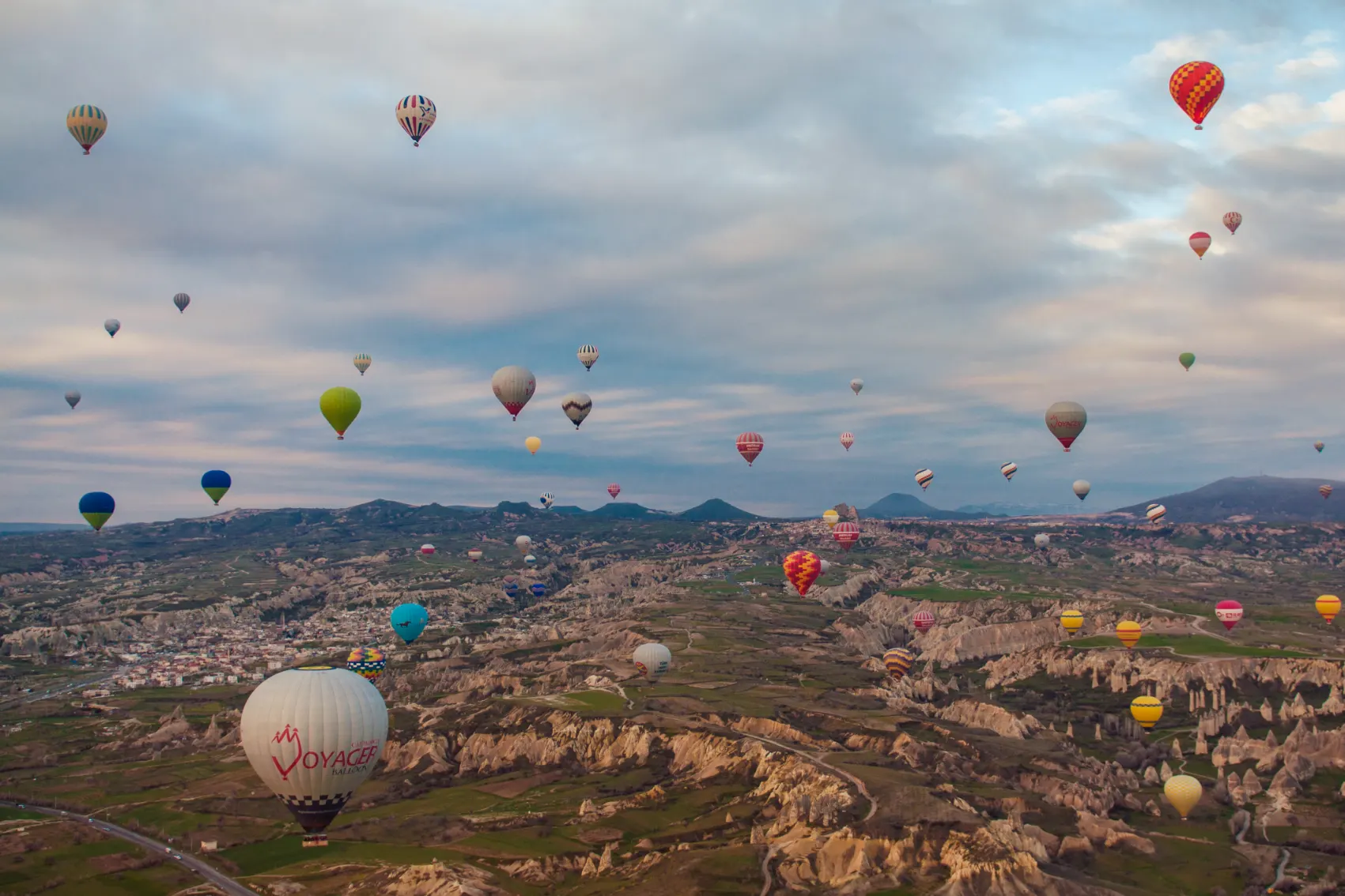 A big gathering of hot air balloons dot the sky with the wonders of Cappadocia, Turkey below