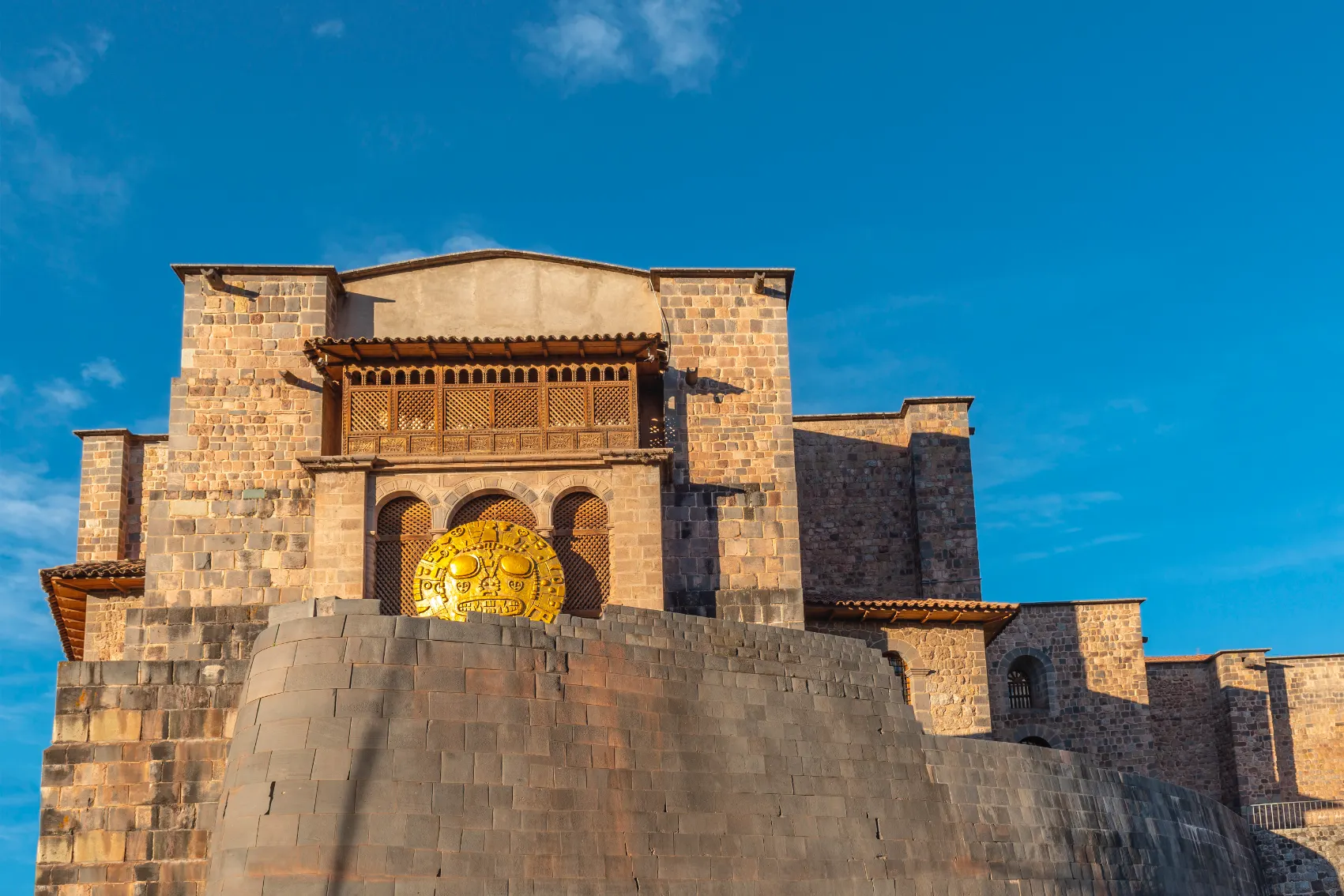 Qorikancha aka the Temple of the Sun looks resplendent against a blue sky with a giant gold sun god replica out front
