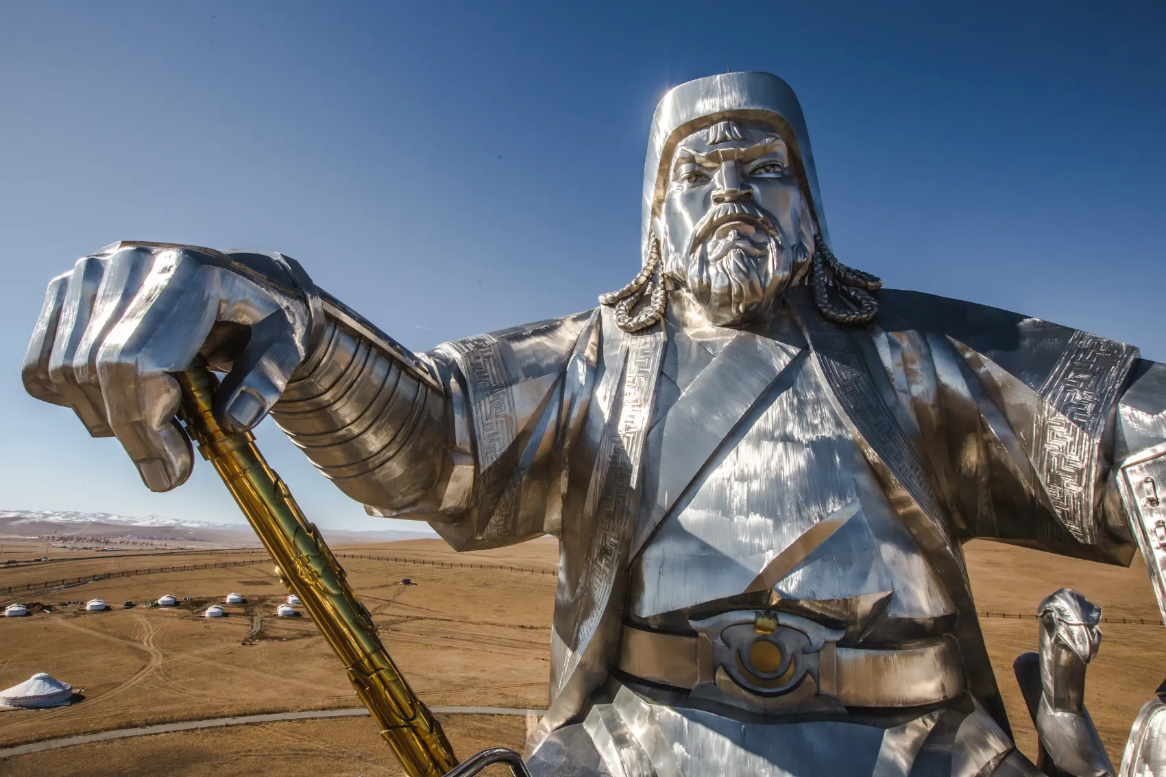 A giant silver statue of Genghis Khan shines with yurts in background of Mongolia