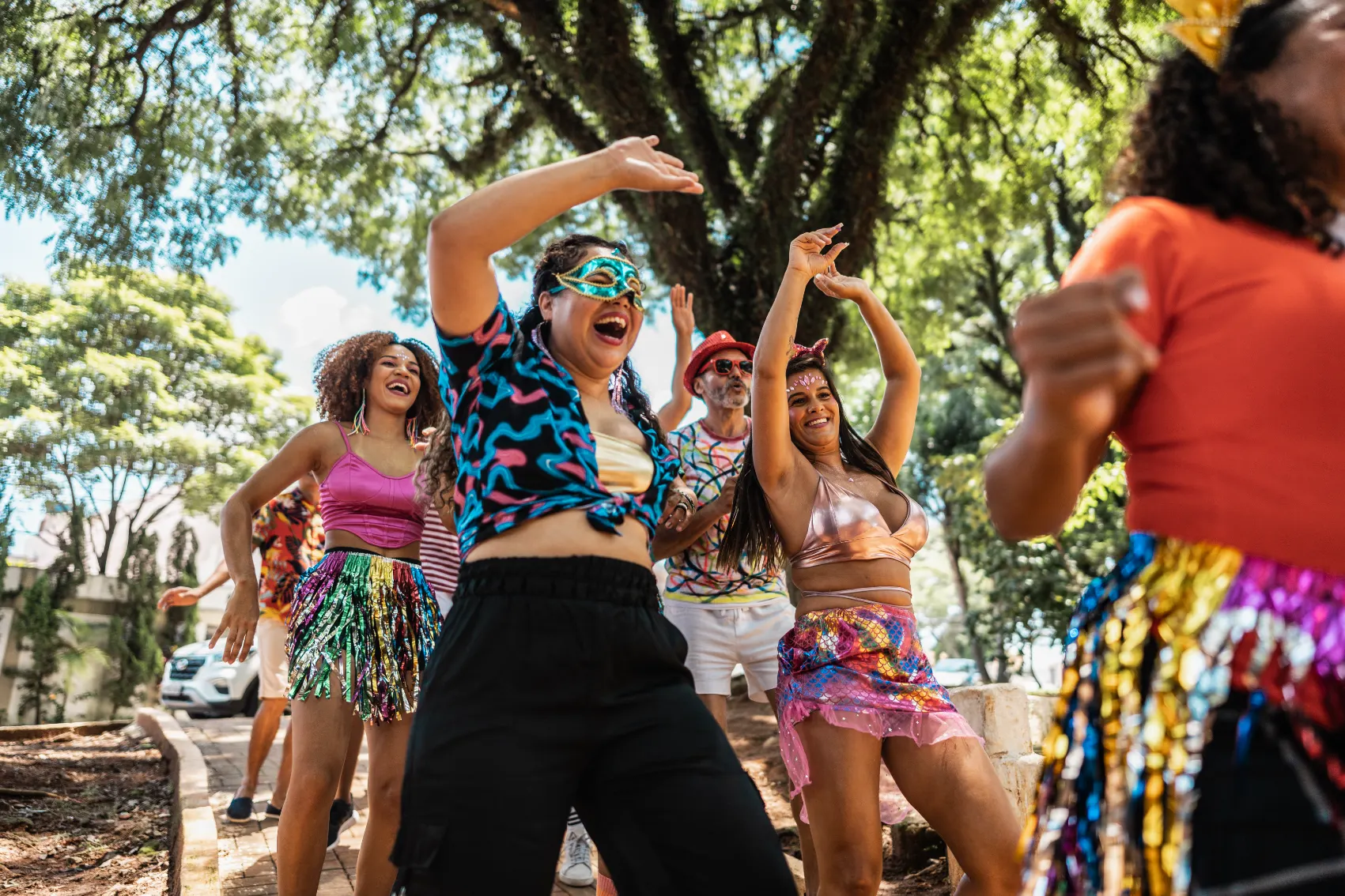 A bunch of colourfully dressed friends in masks dance in the park at arnival in Rio