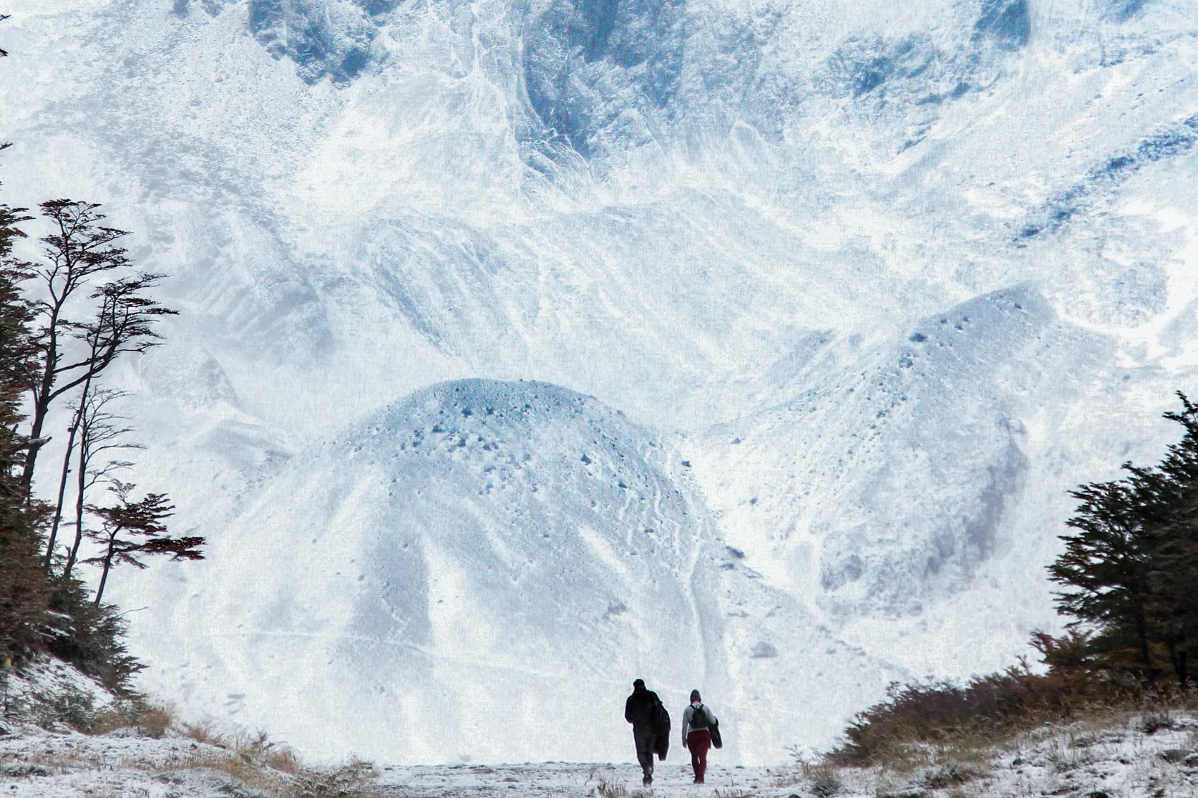 Two people hike in front of the white snow of Glacier Martial in Ushuaia, Argentina