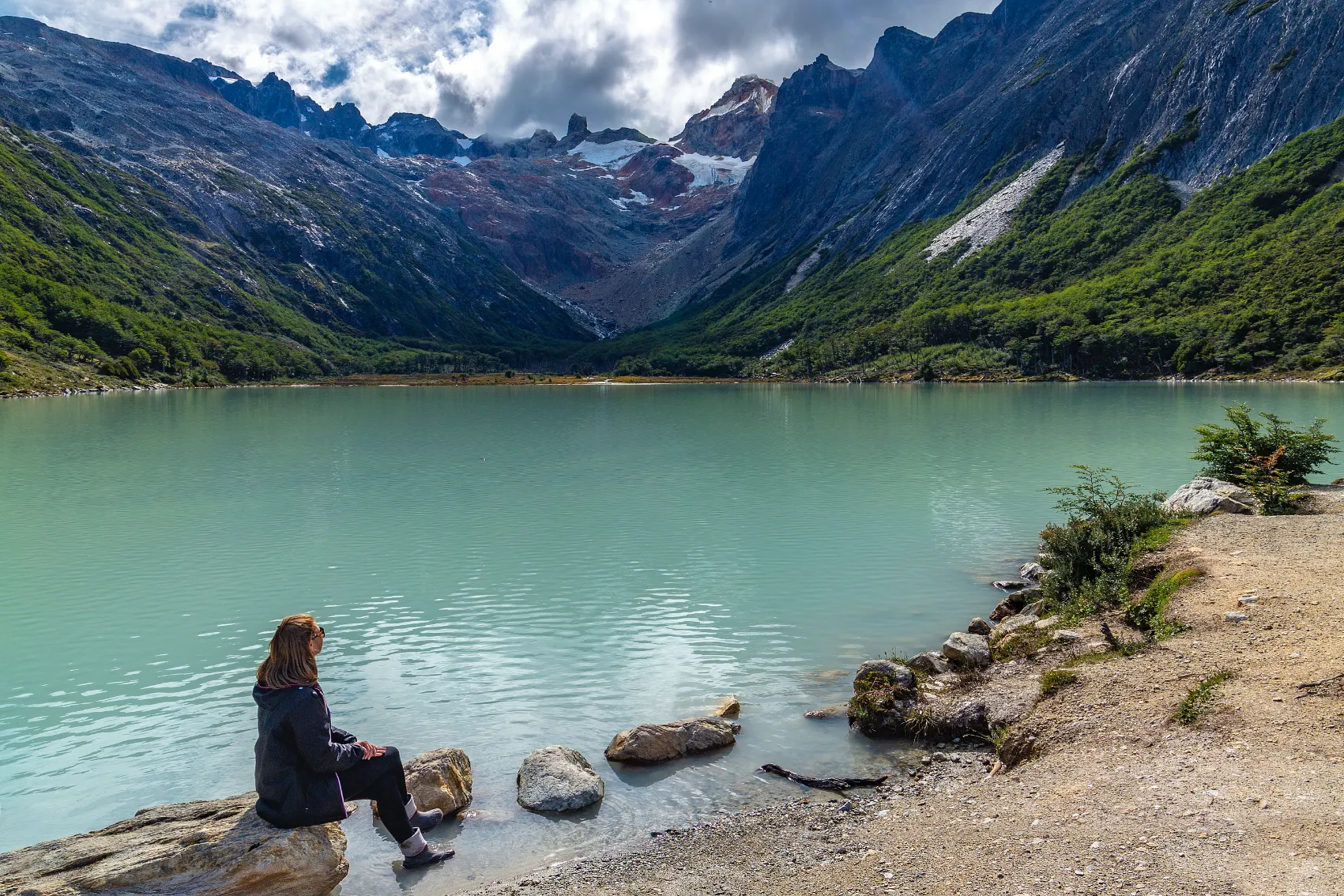 A woman sits on a rock in front of Laguna Esmeralda in Ushuaia, Argentina