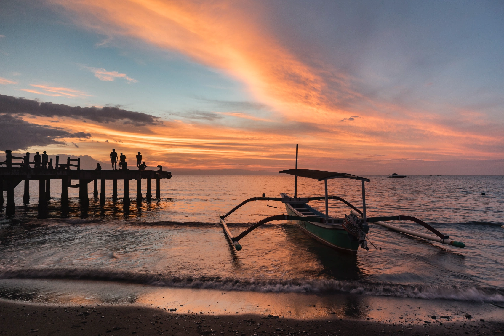 Lovina Beach, Bali People stand on a dock at sunset next to a traditional outrigger boat at Lovina Beach, Bali