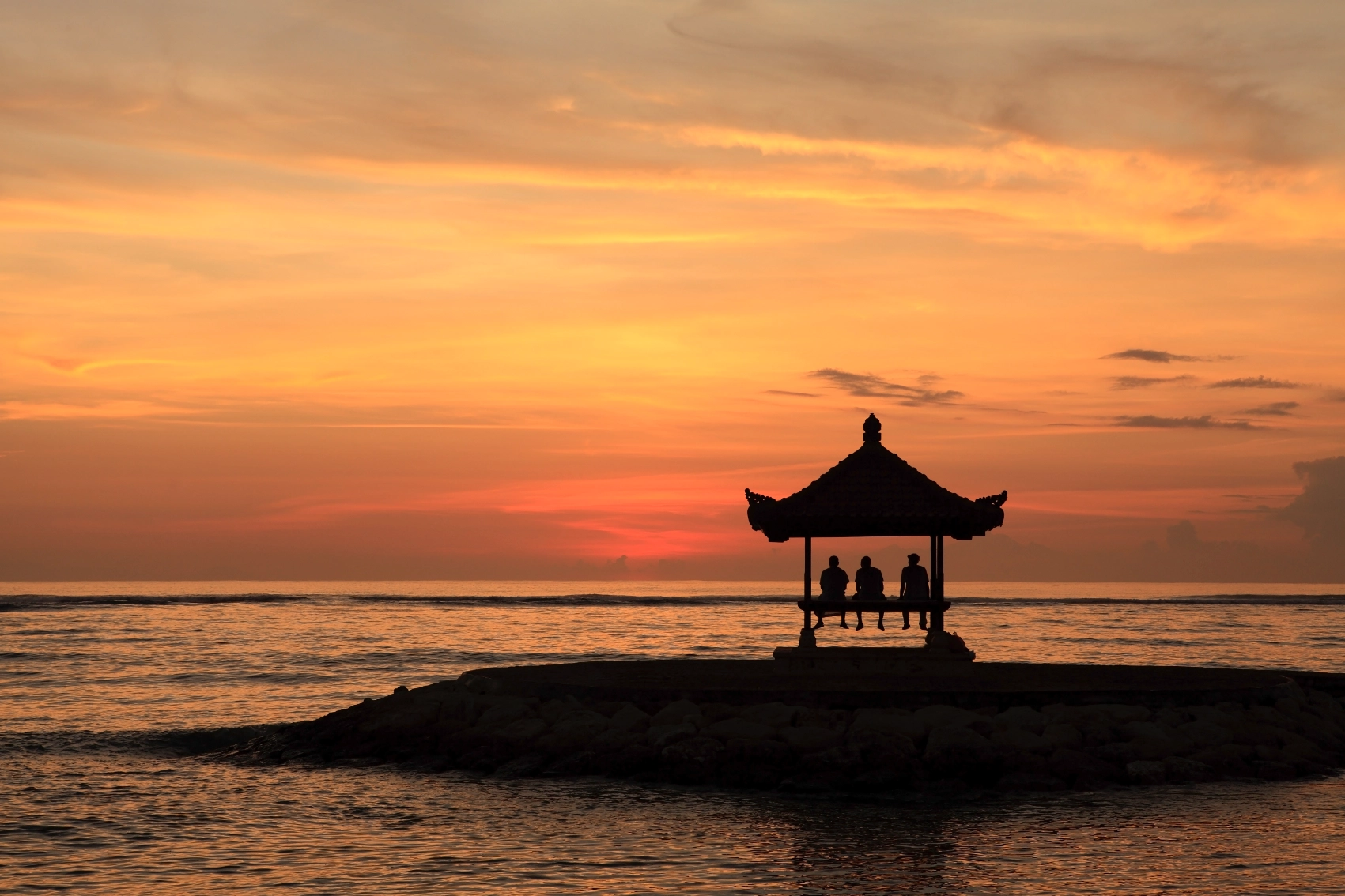 Sanur Beach, Bali Three people sit in a pagoda at sunset on Sanur Beach, Bali