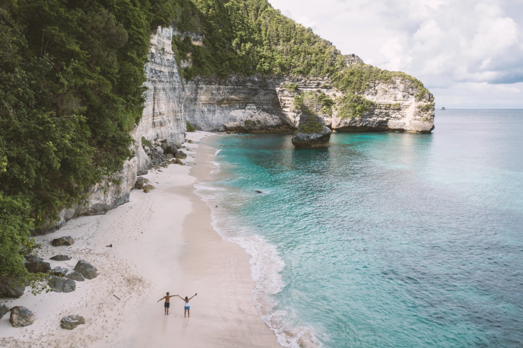Beaches in Bali Bird's-eye view of two people walking on a beach in Bali, with cliffs on one side and the sea on the other