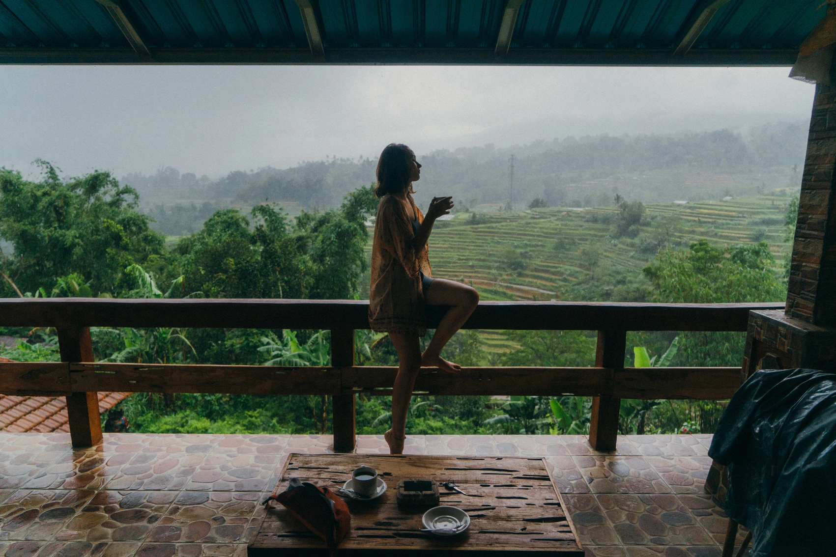 Rainy season in Bali A woman with a mug of tea sits in a pagoda overlooking rice terraces in the rain in Bali, Indonesia