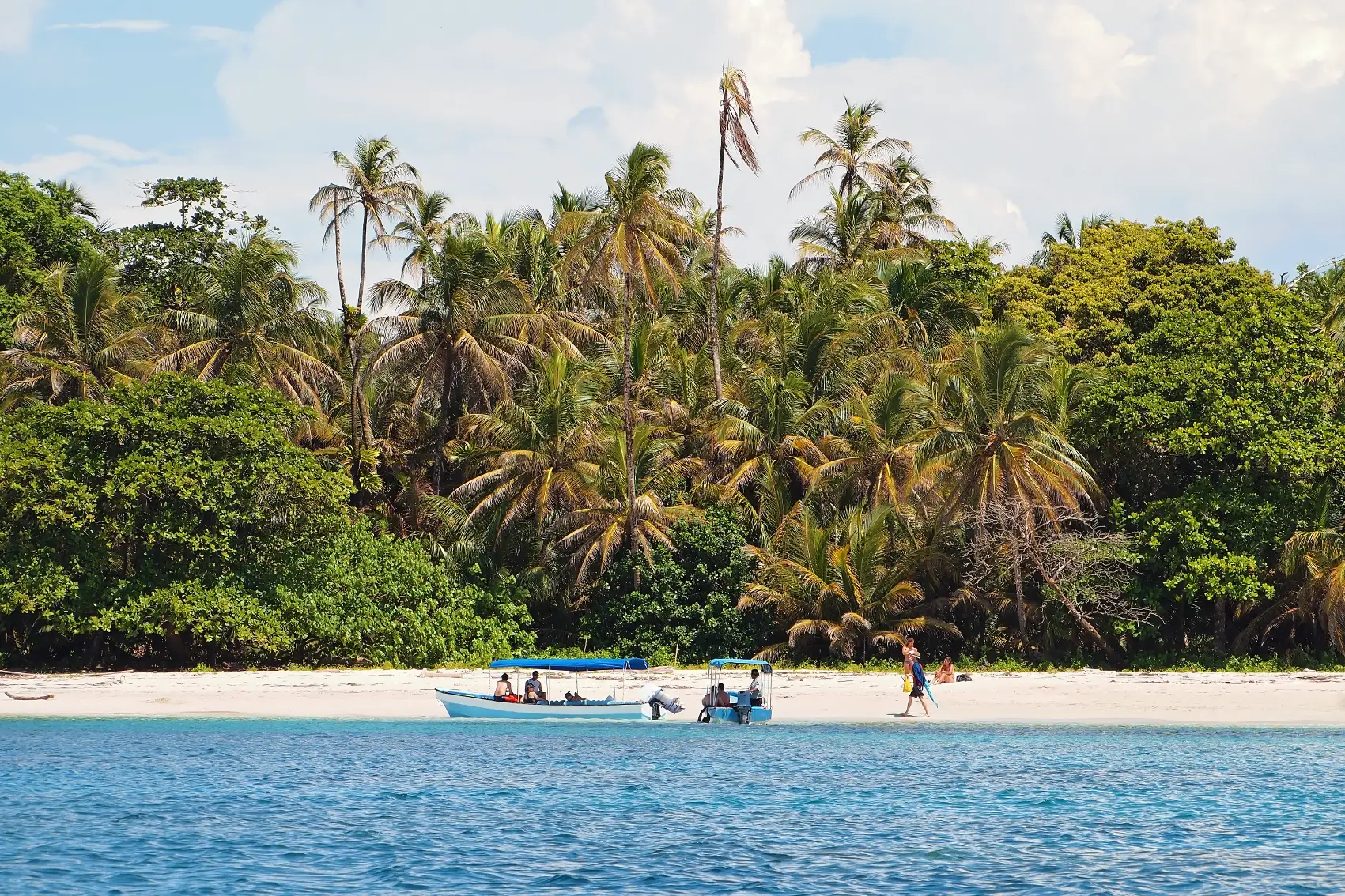 Travellers walk on a sandy beach near a boat on Cayos Zapatilla, Panama