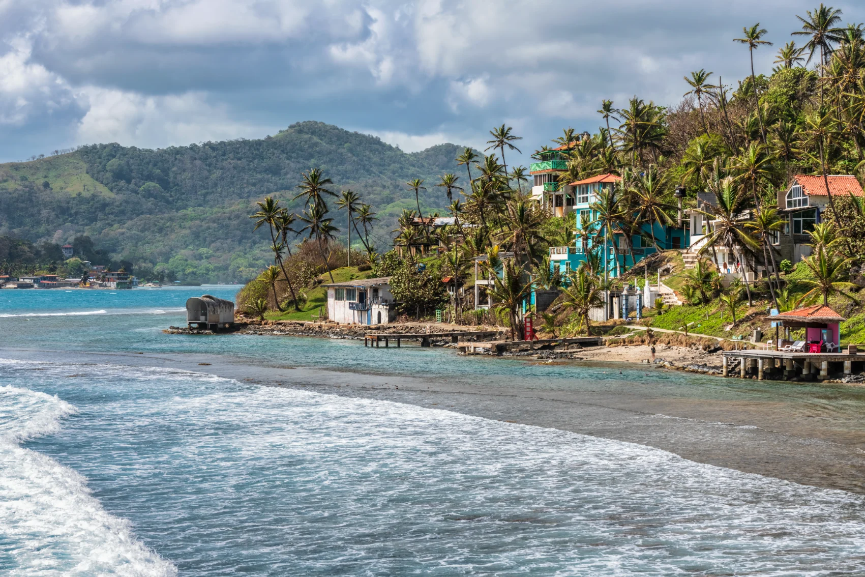 Palm trees, sea, and houses on the shore of Isla Grande, Panama