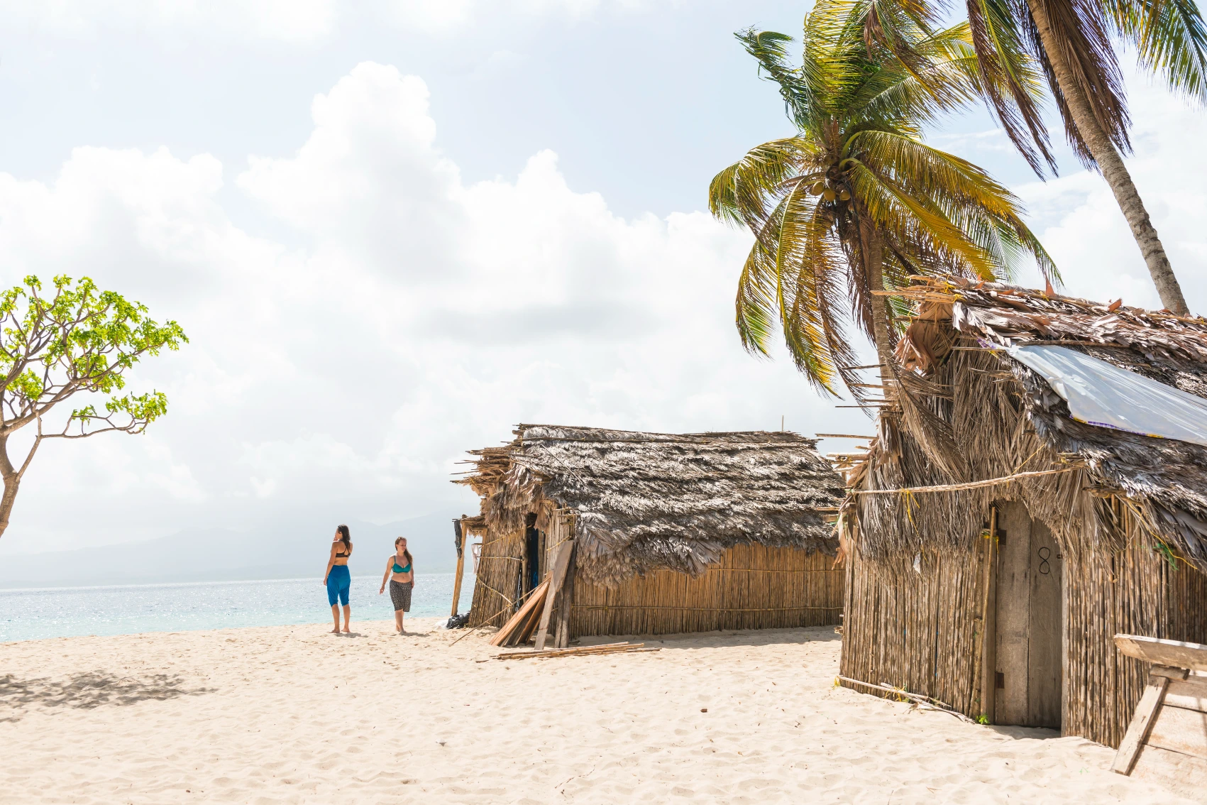 Two people walk near beach huts on the sand of the San Blas Islands, Panama
