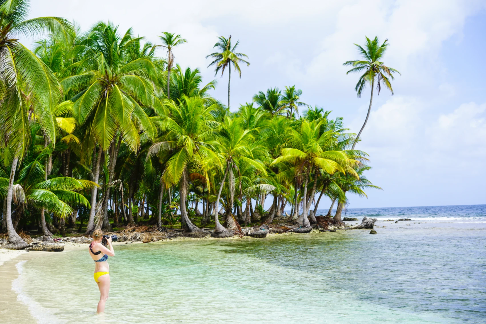 San Blas Islands, Panama A woman holds up a camera to take a photo while standing in the water on the San Blas Islands, Panama