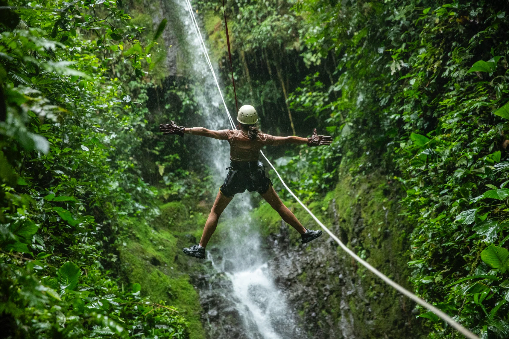 Arenal Volcano, Costa Rica A woman is attached to a canyoneering rope in a narrow gorge surrounded by jungle near Arenal Volcano in Costa Rica