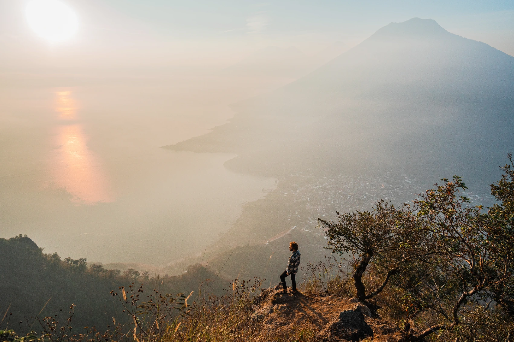 Lake Atitlán hike, Guatemala A male hiker sits on a rock ledge overlooking Lake Atitlán and its volcano at sunset in Guatemala