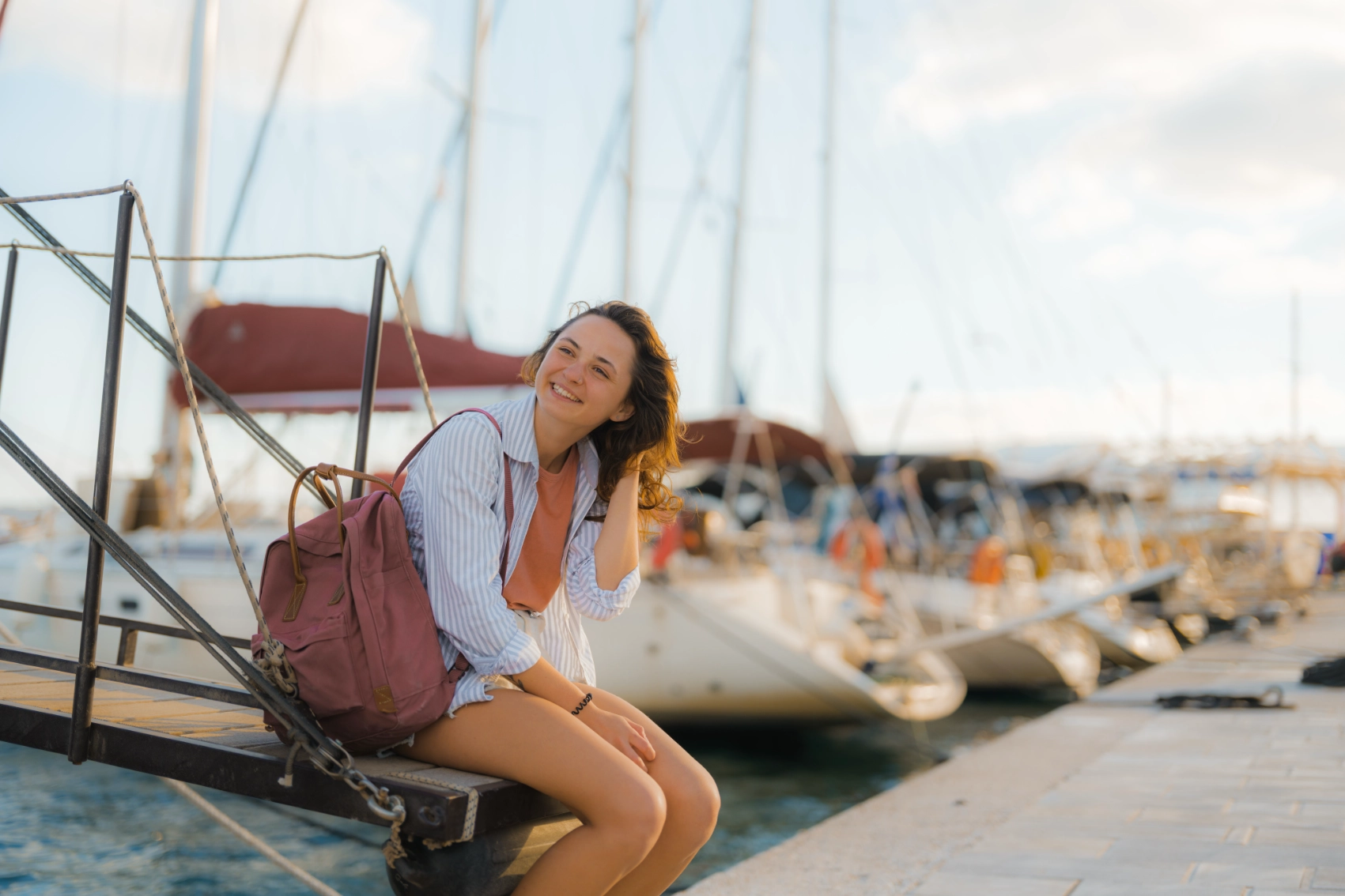 A woman traveller sits at a pier full of yachts in Ios, Greece