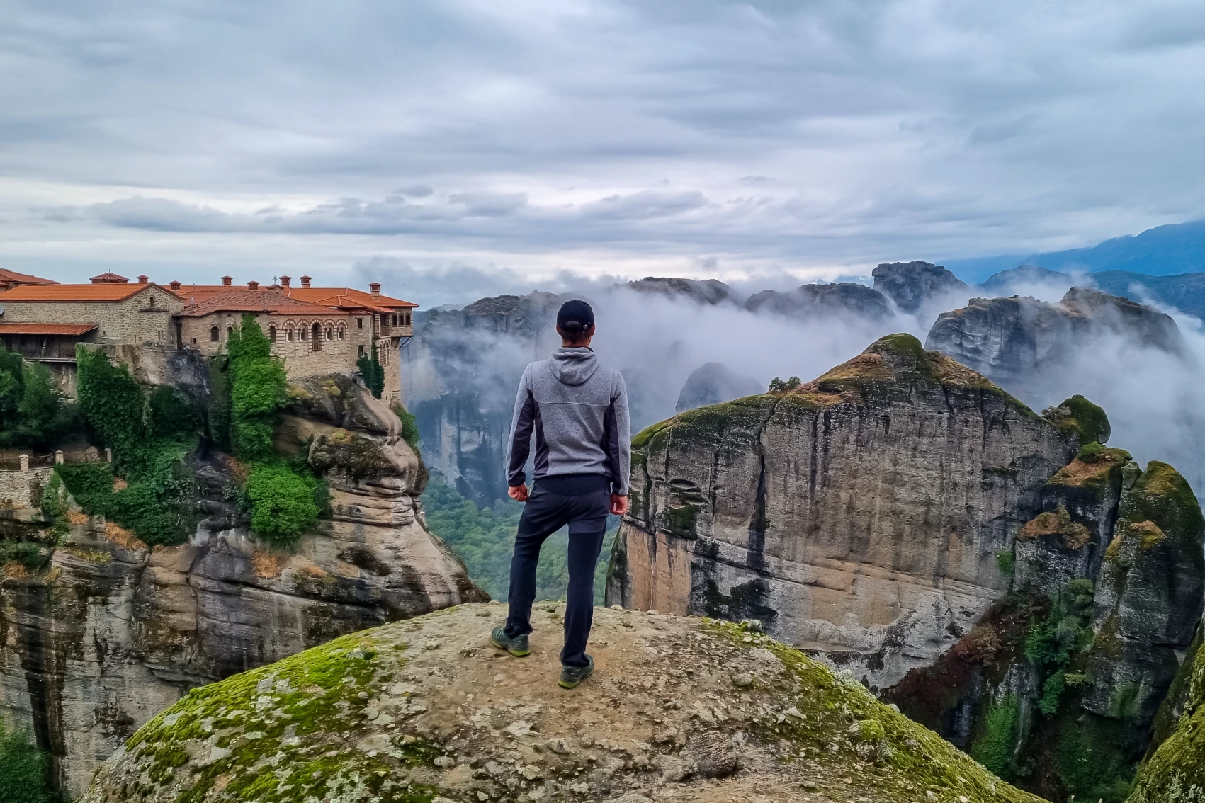 Meteora, Greece A man stands near the cliff edge overlooking a monastery in Meteora, Greece