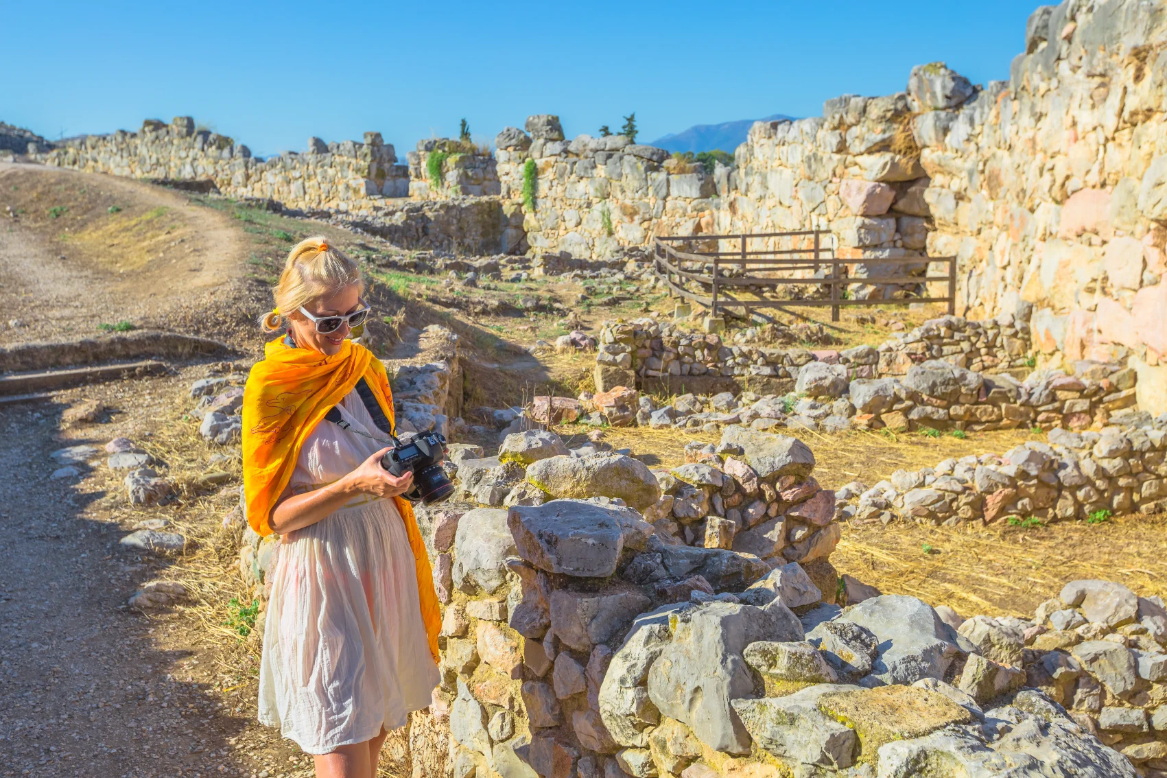 Mycenae, Greece A woman traveller looks at her camera while walking through the ruins of ancient Mycenae, Greece