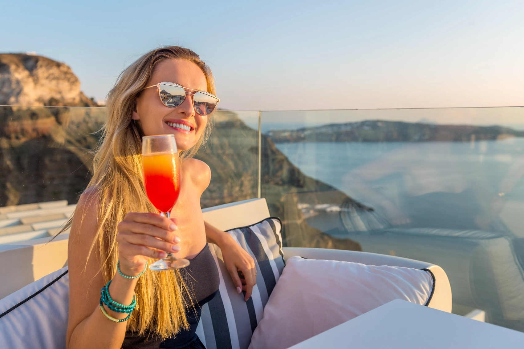 Bars in Santorini A woman traveller drinks a colourful cocktail at a table overlooking the sea in Santorini