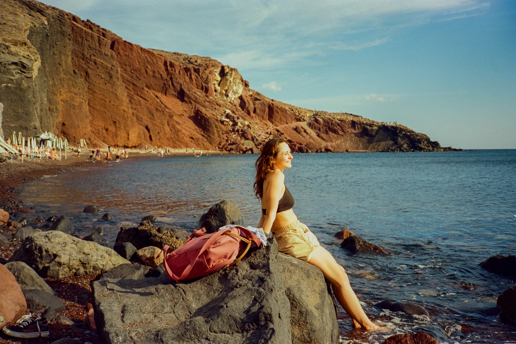 Red Beach, Santorini A woman traveller sits on a rock at Red Beach in Santorini, Greece