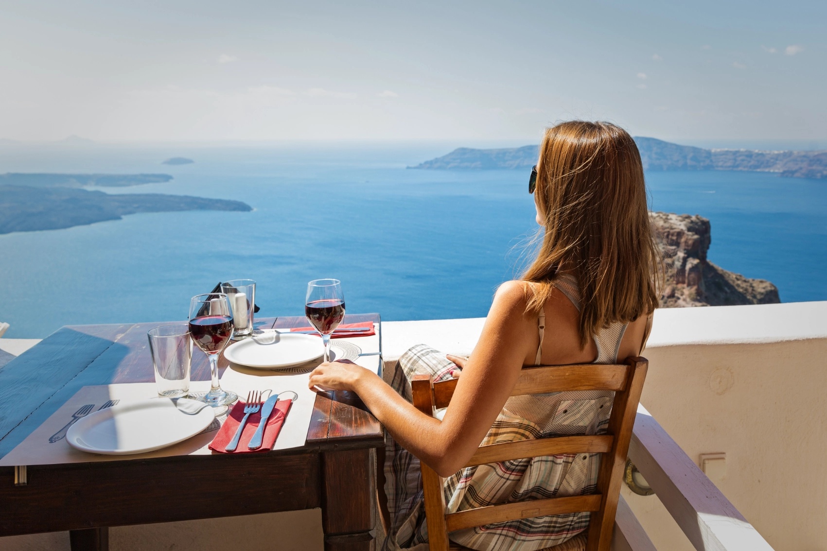 Santorini restaurants A woman traveller sits at a restaurant table overlooking the sea in Santorini