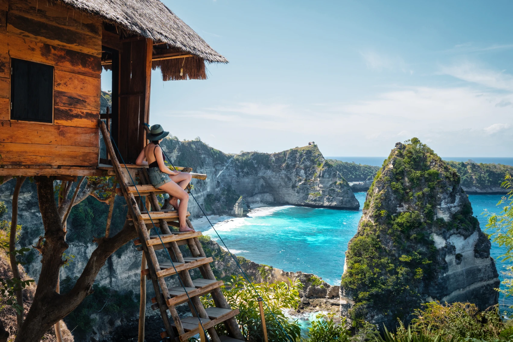 Weather in Indonesia A woman sits on the steps of a treehouse overlooking a beach in Indonesia