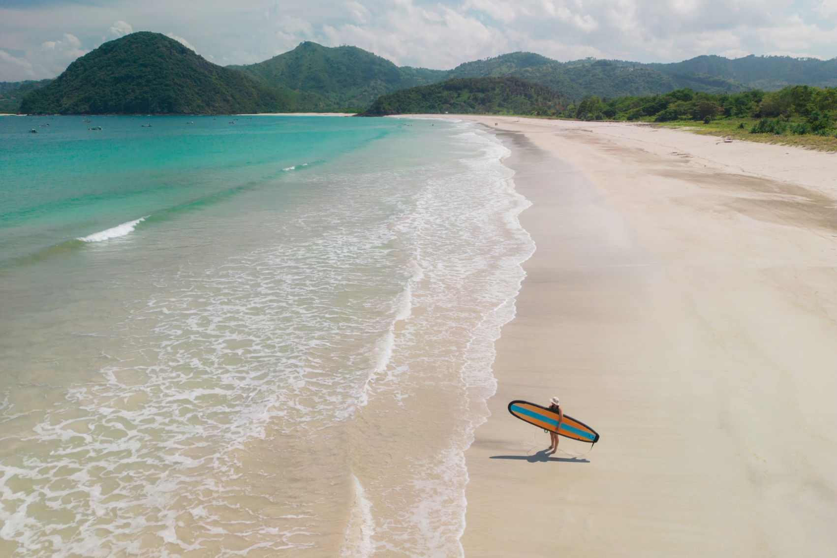 Surfing in Indonesia Aerial view of a surfer standing with his board on a beach in Indonesia