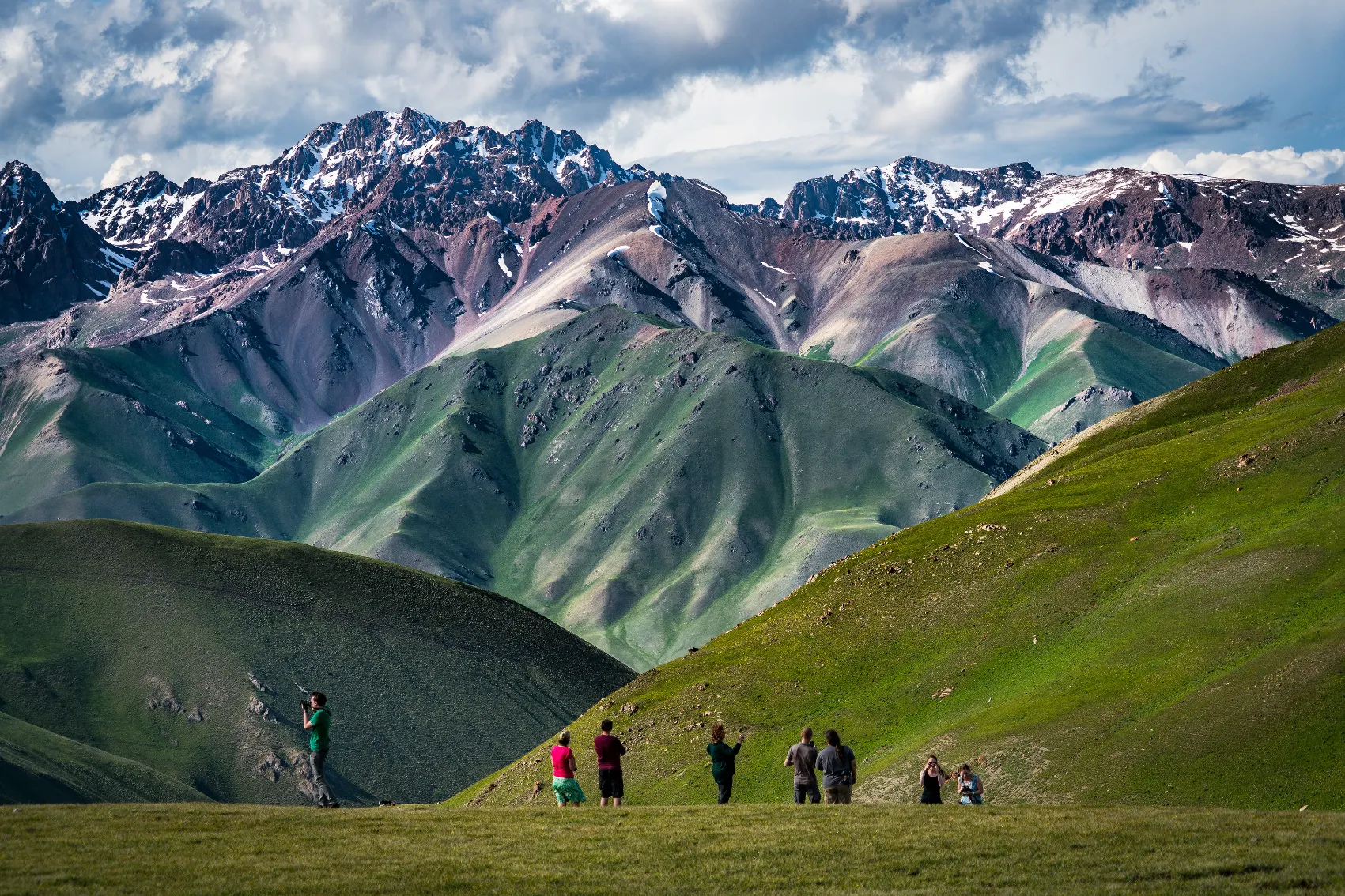 A group of travellers stand in front of purple-green mountains in Song-Köl, Kyrgyzstan