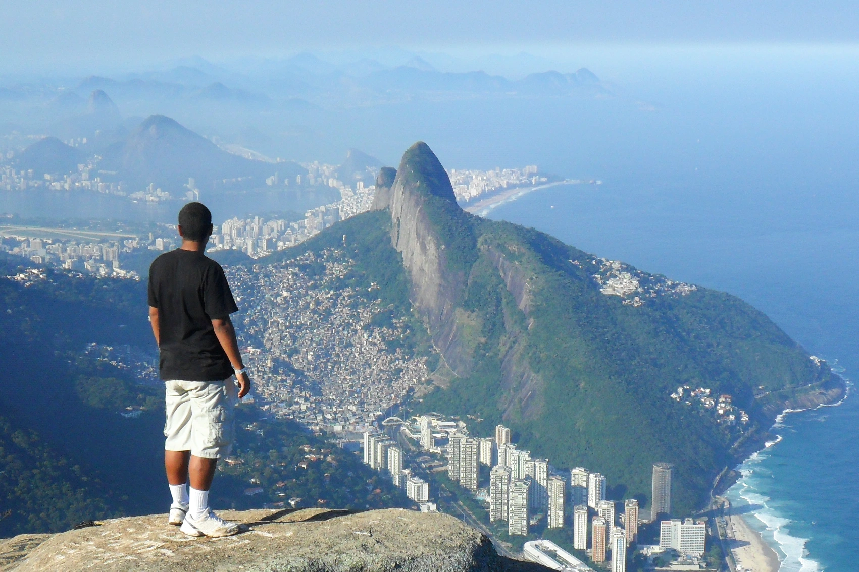 A man stands on a rocky ledge overlooking Rio de Janiero from Tijuca National Park