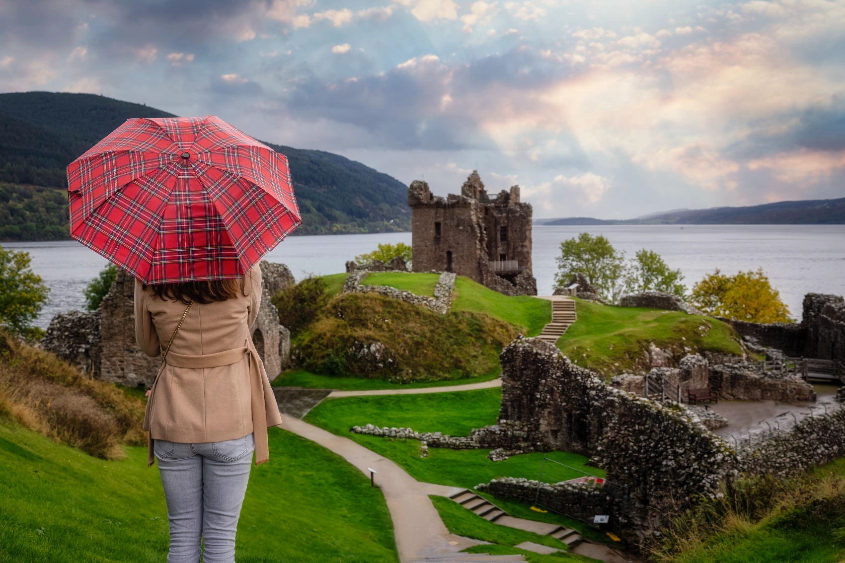 A woman with an umbrella looks at Urquhart Castle in Scotland