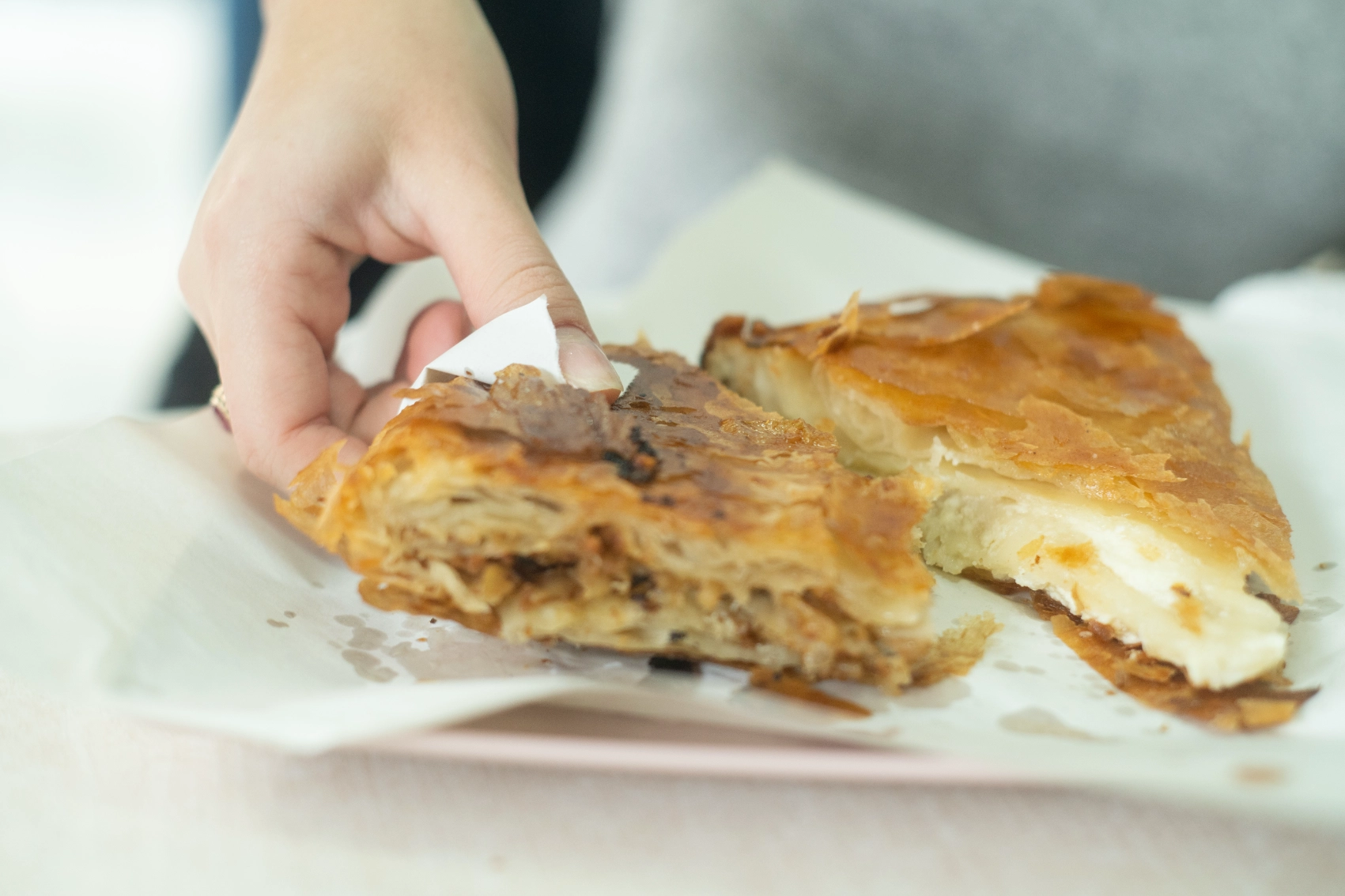 A person's hand picks up a piece of burek sitting on a plate