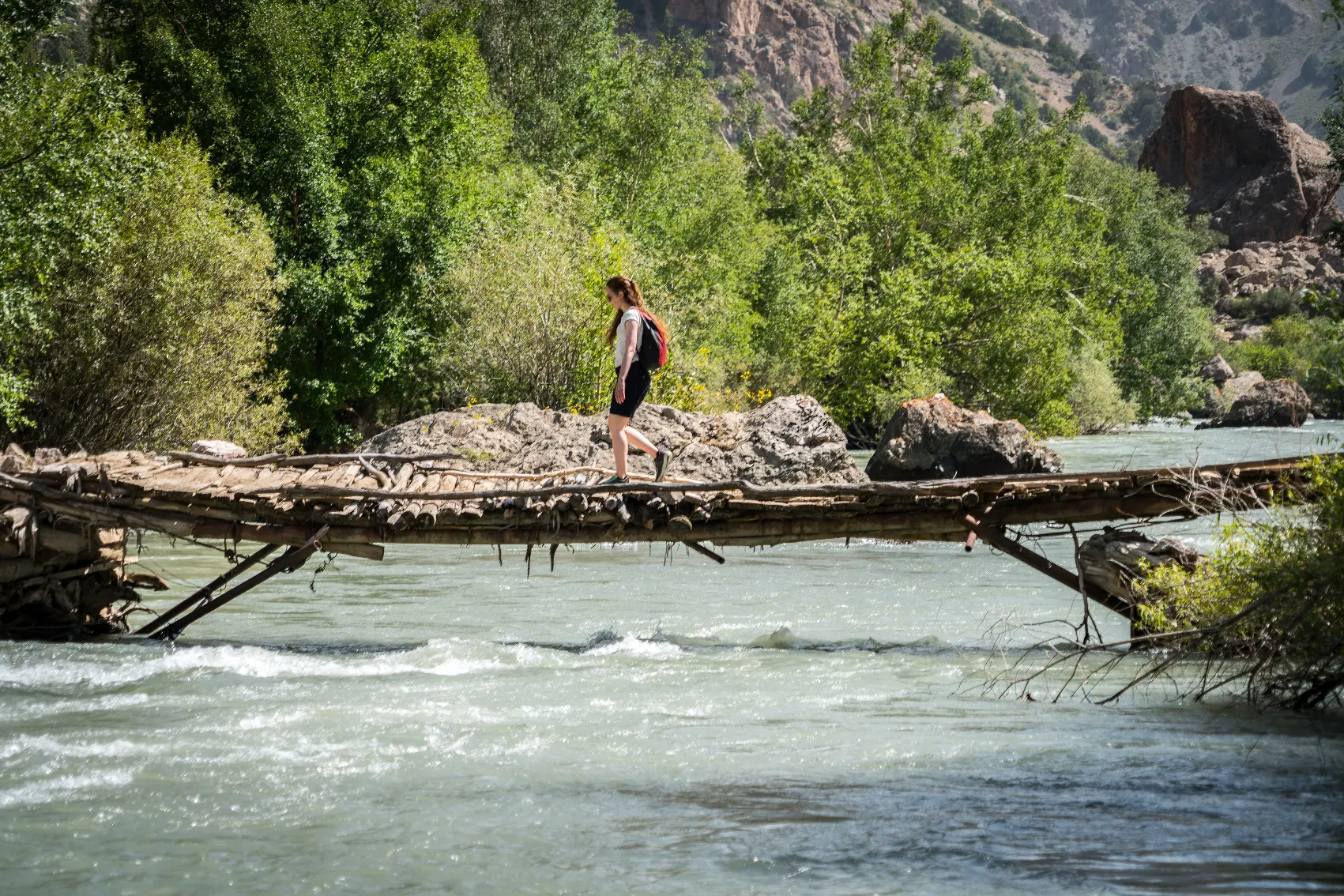 A hiker walks on a wooden bridge above Iskanderkul, Tajikistan