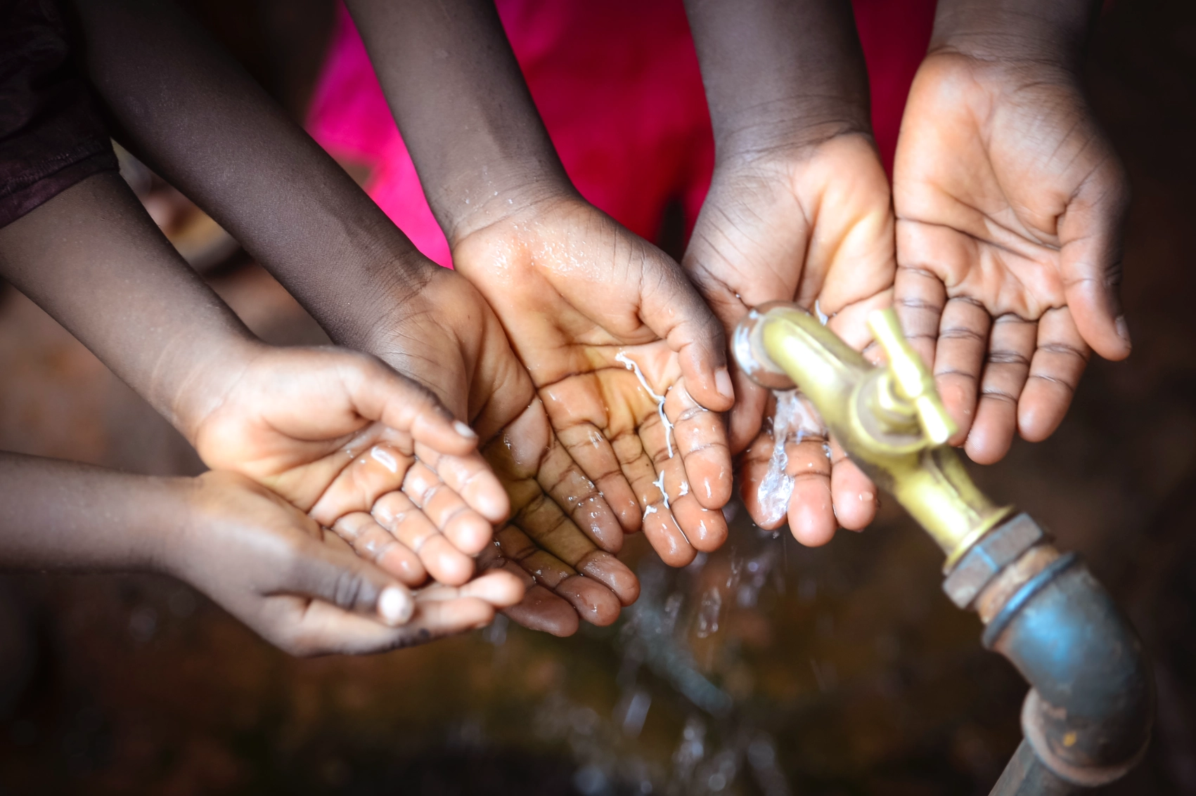 Multiple people wash their hands at a spigot in Benin