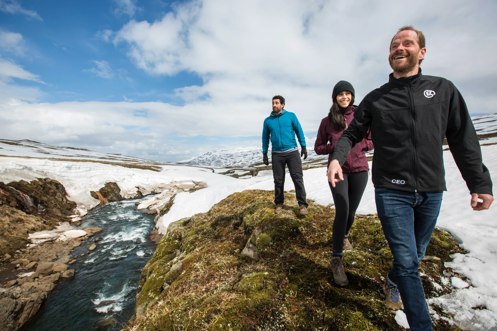 People walk near a stream surrounded by snow in Iceland