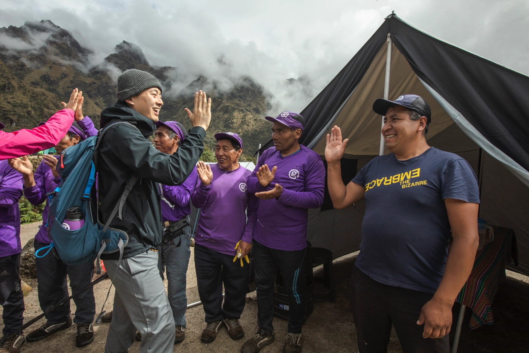 A man high-fives a row of porters in front of a tent on the Inca Trail in Peru