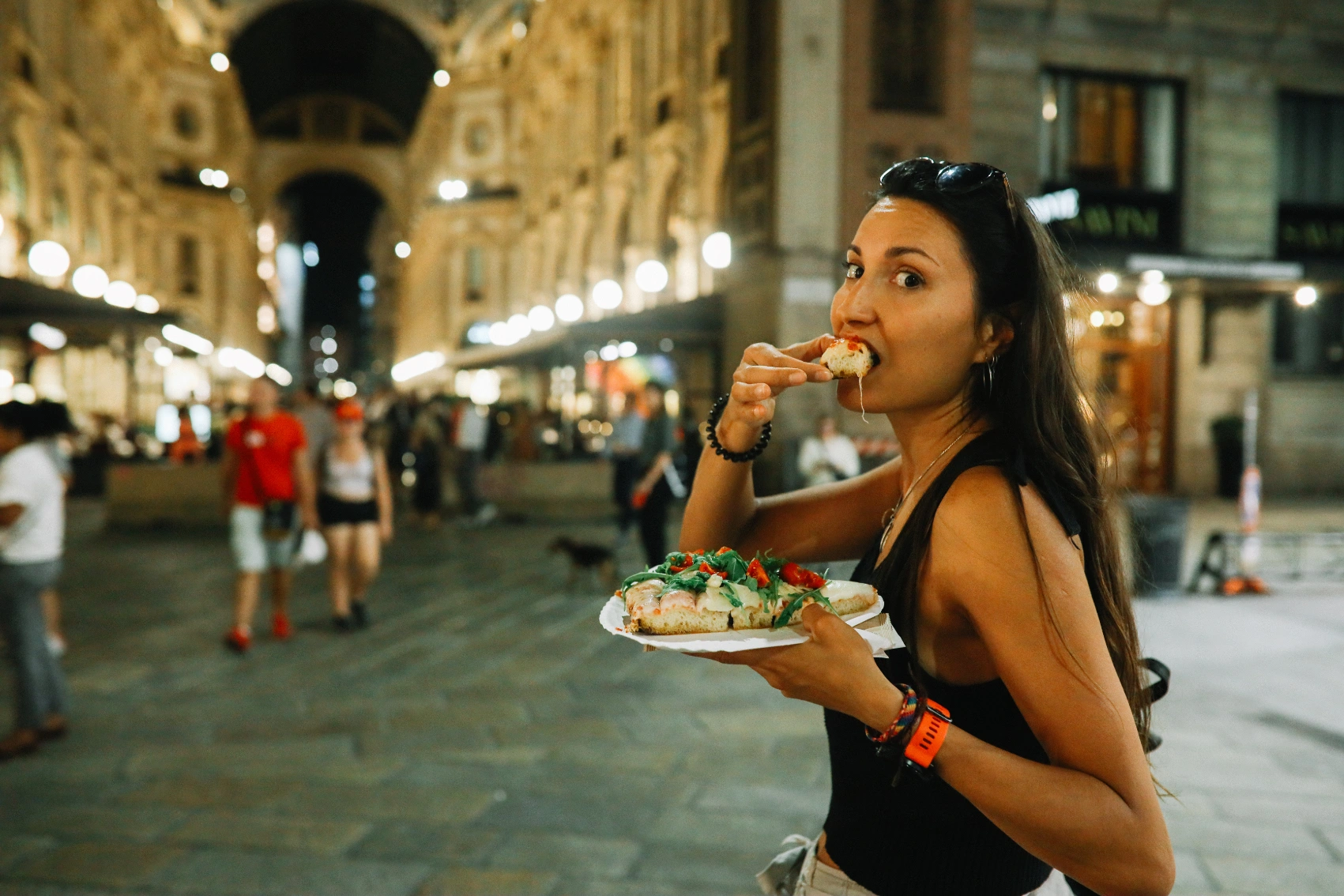 A female traveller stands with a pizza in her mouth in a city in Italy