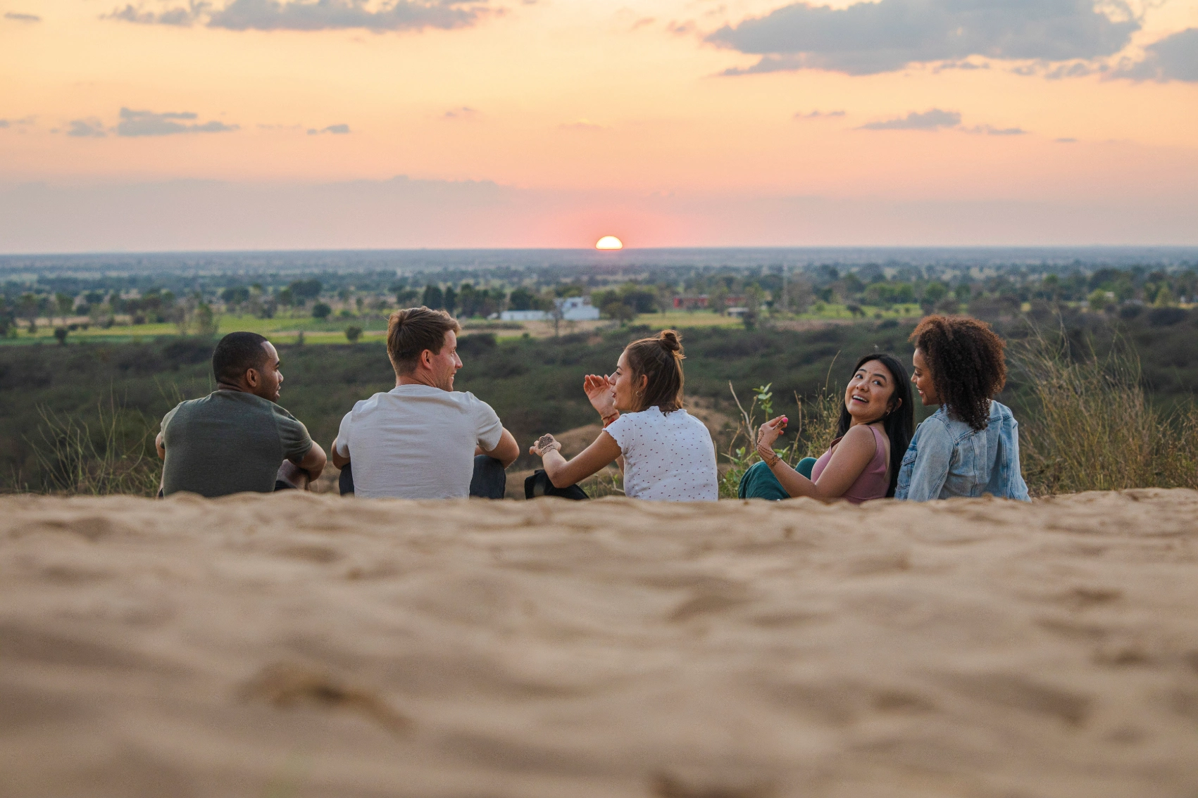 A group of travellers watches the sunset from a dune in India