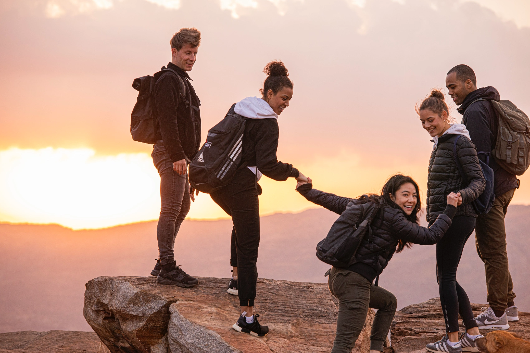A group of travellers helps a fellow hiker up a rocky outcrop in India