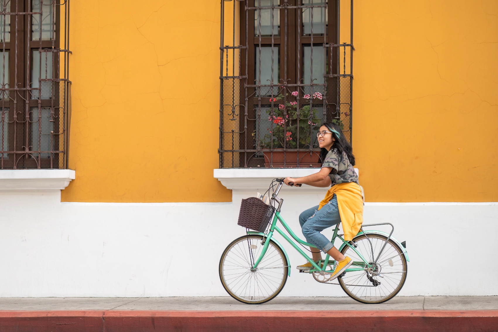Antigua, Guatemala A female traveller rides a bicycle in front of a colourful building in Antigua, Guatemala