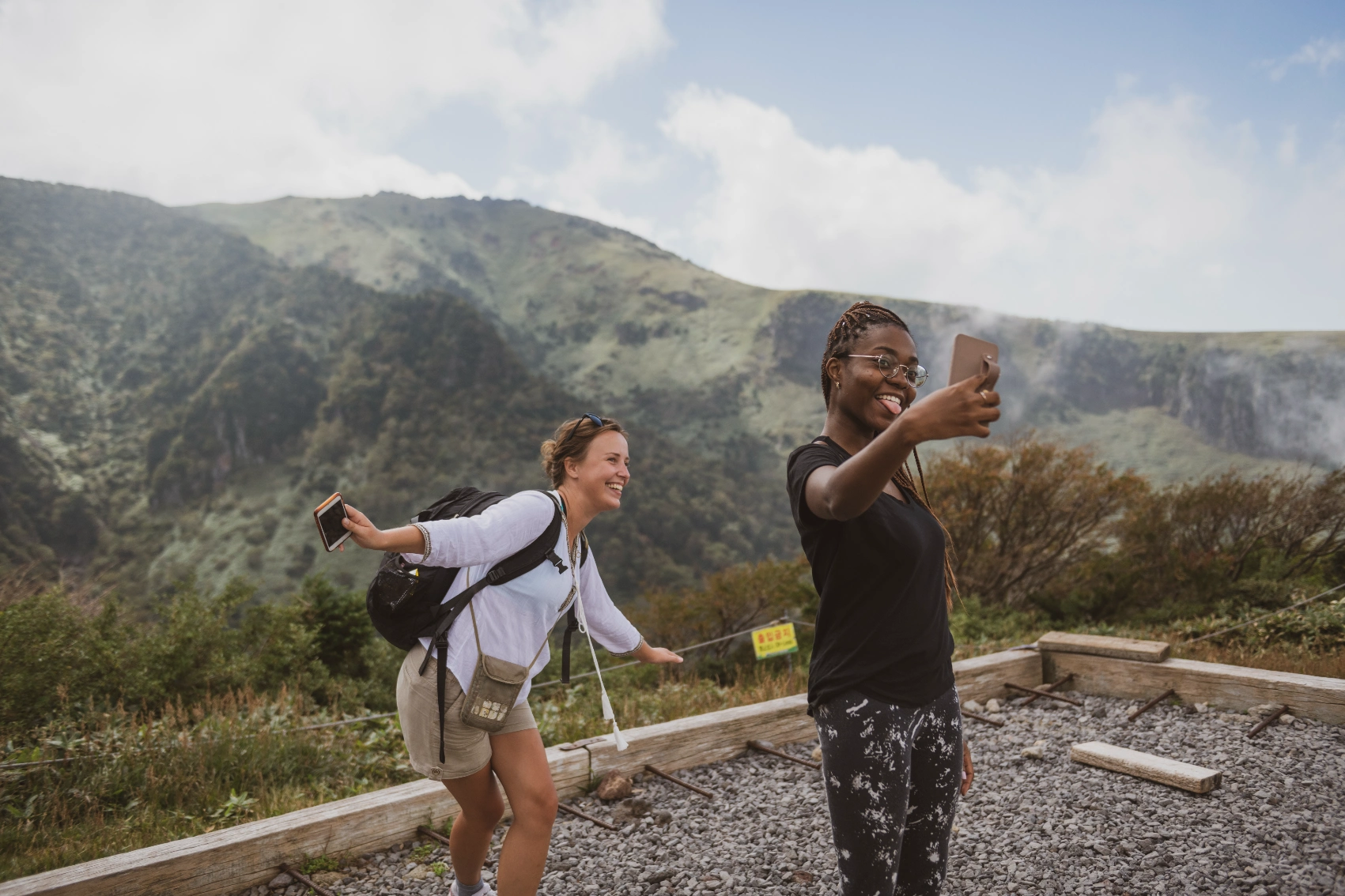 Two female travellers smile for a selfie while hiking on Jeju Island, South Korea